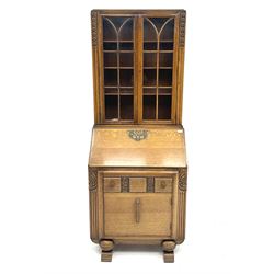 Early 20th century carved oak bureau bookcase, two glazed cupboard doors revealing adjustable shelving, fall front writing desk revealing fitted interior, above one short drawer and single cupboard door, turned ball supports and sledge feet