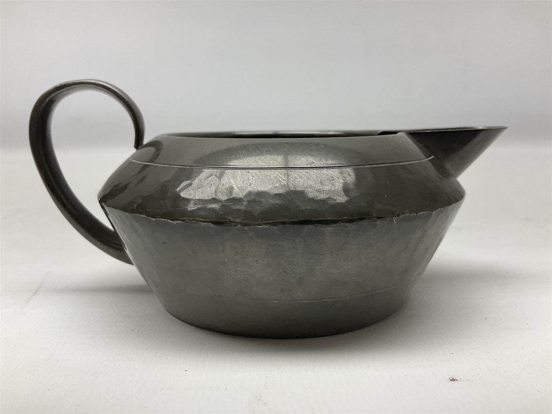 Liberty & Co Tudric pewter three piece tea service, comprising teapot with woven reed handle, twin handled open sucrier, and milk jug, each of squat form with planished finish, each impressed beneath Tudric Pewter Ware 01537 Made in England, together with a matched unmarked tray