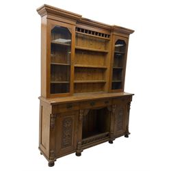 Late 19th century pine dresser, the projecting cornice with dentil and spindle moulded frieze above a three-tier plate shelves, flanked by glazed doors, the base fitted with three frieze drawers over arched apron and carved floral panelled cupboard doors, raised on turned feet