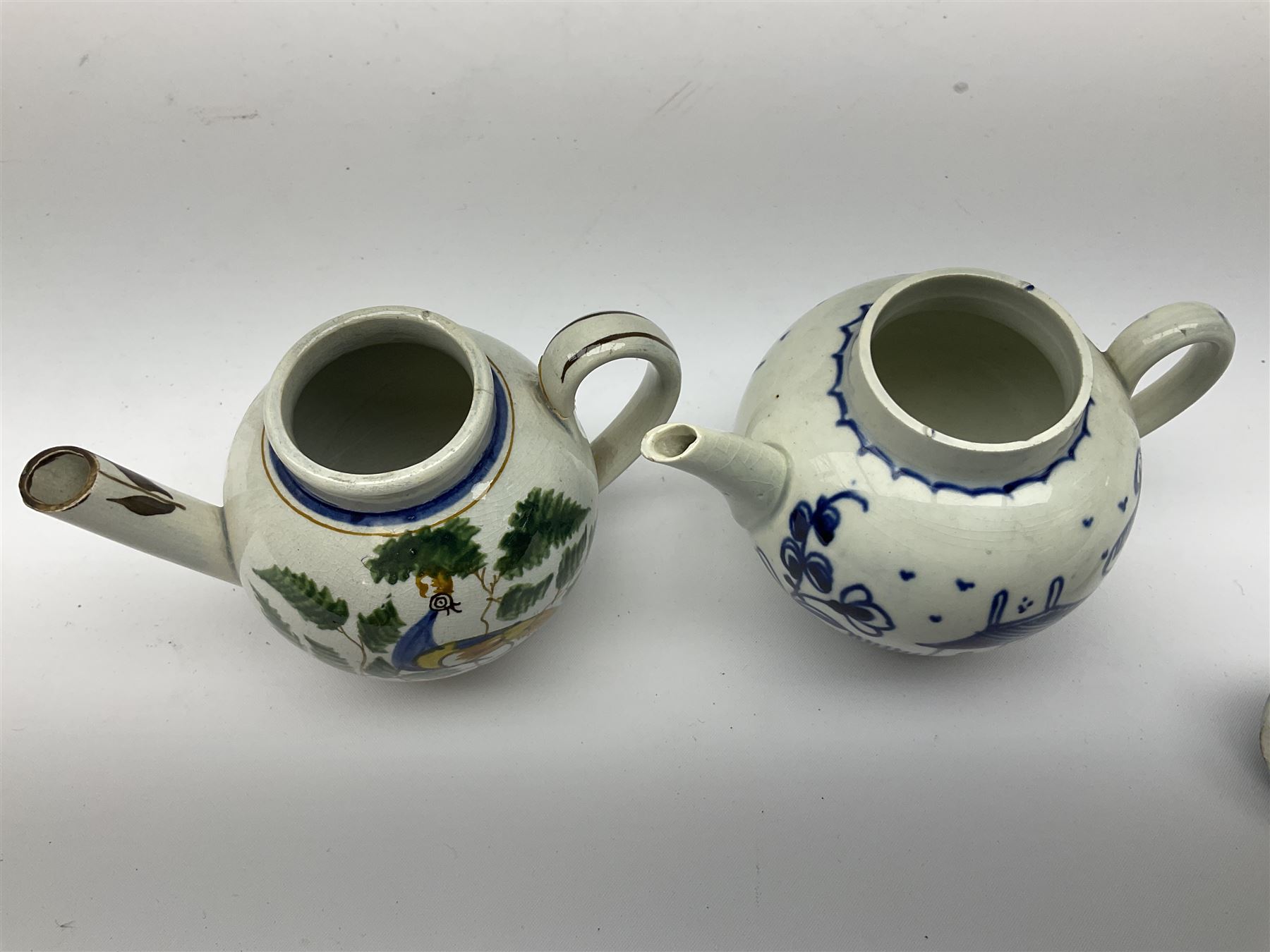 Two 18th century miniature or toy pearlware teapots, the first example lacking cover decorated with an exotic bird, the second with cover painted in underglaze blue with hut and fence, second example approximately H8cm