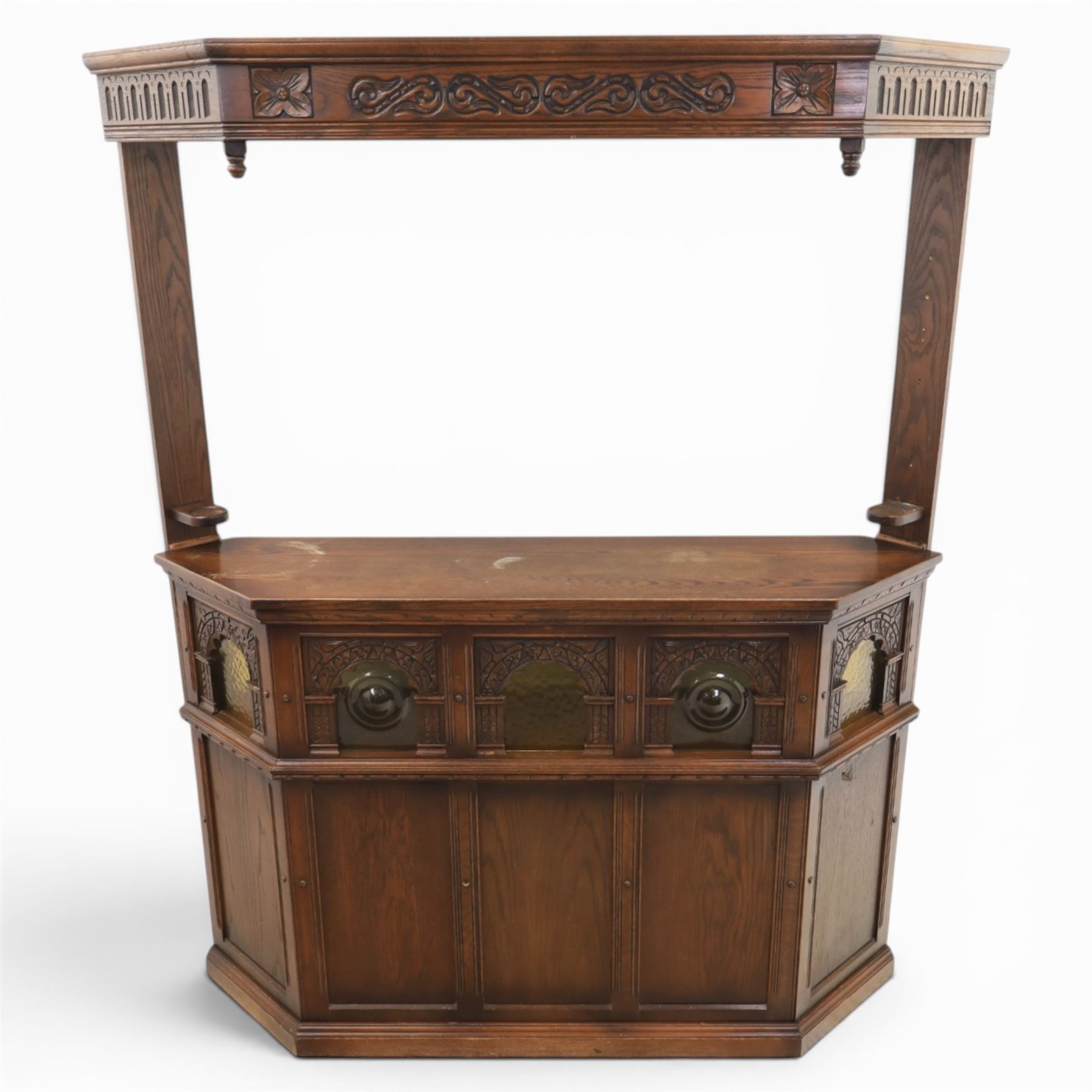 Old Charm - carved oak bar with three bar stools and associated Old Charm drinks cabinet, carved top with channels for glassware beneath, bar surface above glazed panels, shelves for glassware to the back, associated Old Charm drinks cabinet with fall front linenfold carving, above twin doors with shelved interior