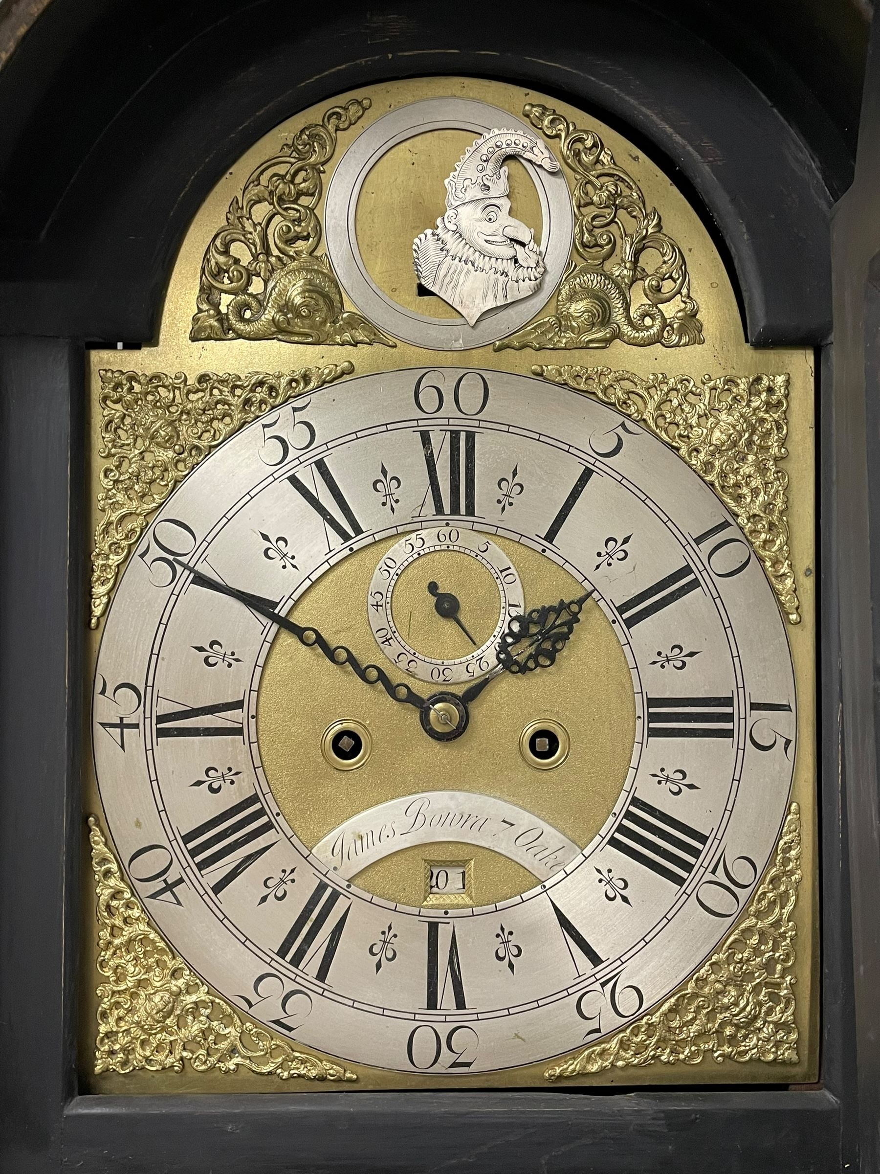 James Bowra of Sevenoaks Kent - 18th century 8-day ebonised longcase clock with gilt decoration c1740, with a flat top, dentil moulding beneath and shaped back splats, break arch hood door flanked by plain pilasters with wooden capitals, long trunk with a curved topped door, on a square plinth with canted corners and raised on a moulded base, brass dial with cast spandrels and a silvered 'Punch' automata to the arch, matted dial centre with seconds ring and date aperture, silvered chapter ring with Roman numerals, five minute Arabics, minute and quarter hour tracks, with matching steel hands and silvered makers name plate, rack striking movement with a recoil anchor escapement, striking the hours on a bell. With weights and pendulum.