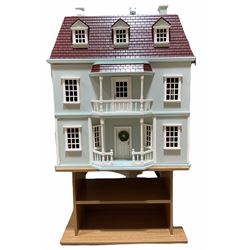 Wooden double fronted three-storey dolls house with pale blue stucco finish and simulated tiled roof, the central recessed front door with balustraded veranda and balcony above, single hinged front opening to reveal four fully decorated rooms and attic room with hinged roof access, fully furnished with quality wooden furniture and comprehensive range of accessories, and seven family member dolls H75cm W64cm D40cm; with oak finish two-tier stand (2)