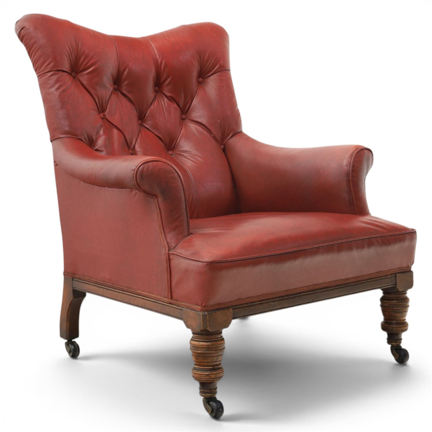 Early 20th century style oxblood red leather Chesterfield armchair, deep buttoned shaped back over padded scroll arms and loose seat cushion, raised on turned mahogany front supports with brass caps and castors