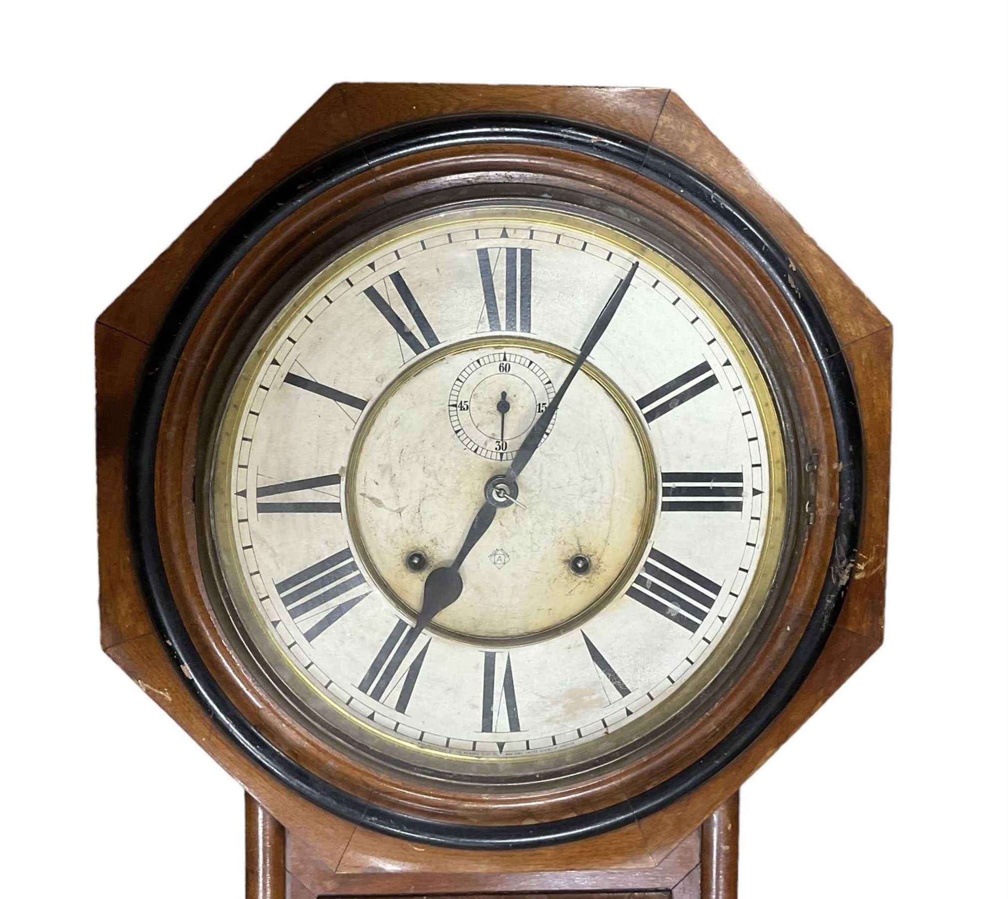 American - Late 19th century Ansonia 8-day wall clock, with a hexagonal wooden dial surround and circular spun bezel, glazed case door and visible pendulum,  two part dial with Roman numerals, minute track, spade hands and seconds dial, twin train spring driven movement striking the hours on a gong.