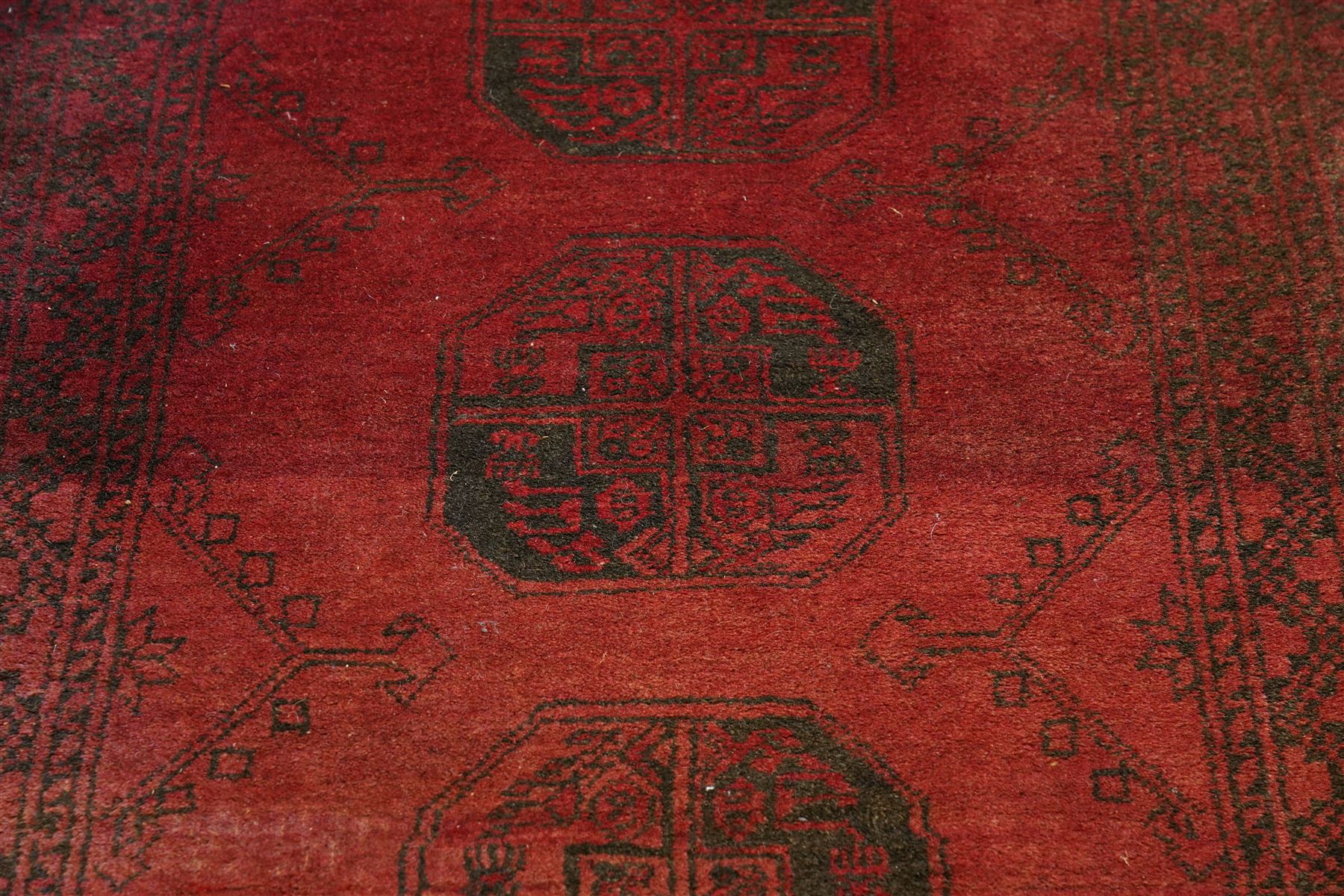 Antique Persian Bokhara red ground runner rug, repeating Gul pattern, surrounded by borders, with fringed ends