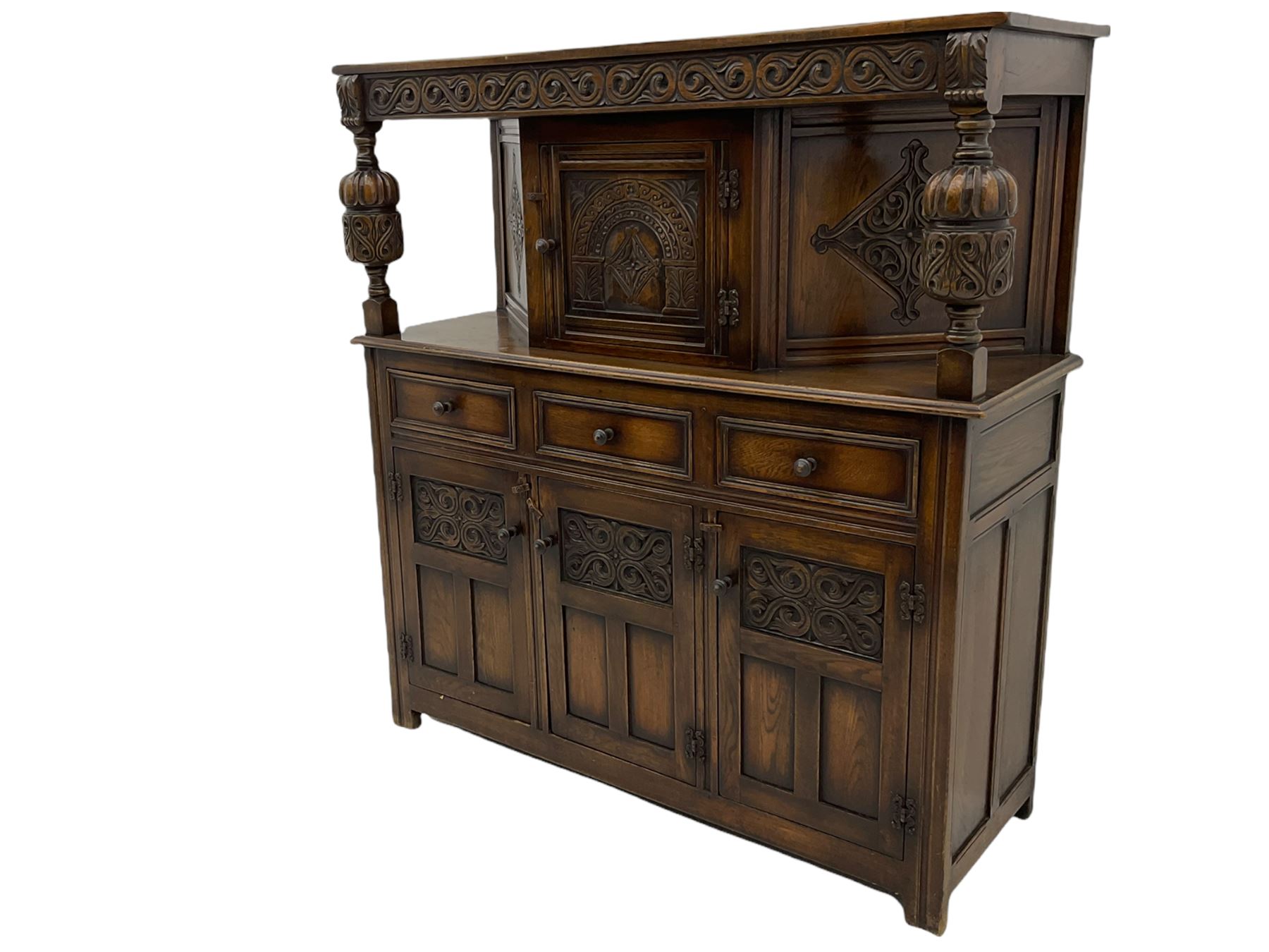 20th century carved oak court cupboard, s-scroll carved frieze over panelled cupboard door carved with arch, lobe and scroll carved cup and cover supports, fitted with three drawers and three cupboards below
