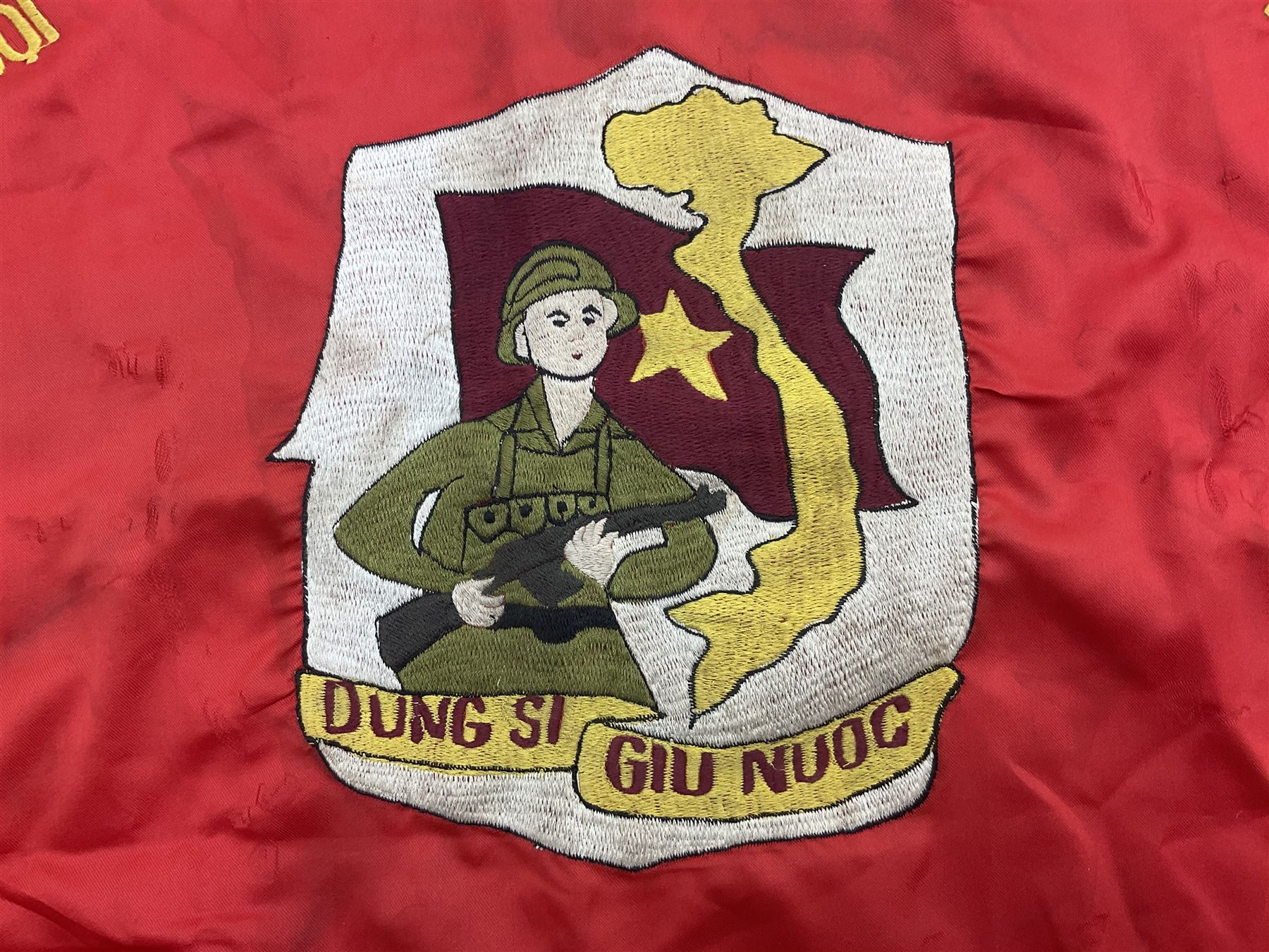 1960s North Vietnam banner embroidered in yellow thread on a red ground, roughly translates as 'Peoples Army of Viet Nam. Warriors of Viet Nam Determined To Keep The Country 1964' around a central military crest with the motto 'Warriors Keep The Country'; tassels to three sides 70 x 100cm
