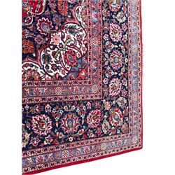Large Persian Kashan crimson ground carpet, central floral medallion surrounded by swirling leafy branches and palmettes, enclose by floral pattern spandrels, the indigo border with overall scrolling design decorated with palmettes, within guard stripes 