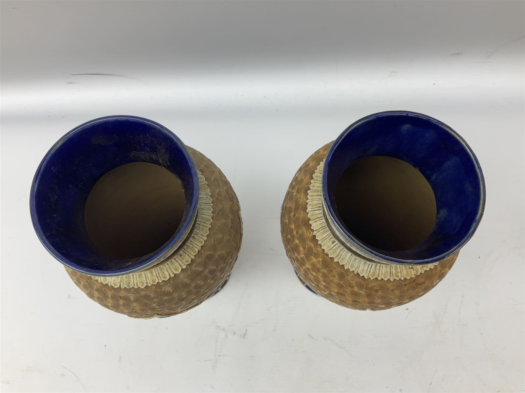 Pair of Royal Doulton Lambeth stoneware baluster vases, decorated in light relief with panels of foliage on blue ground, with gilt scrolls above, impressed mark beneath, 28cm high