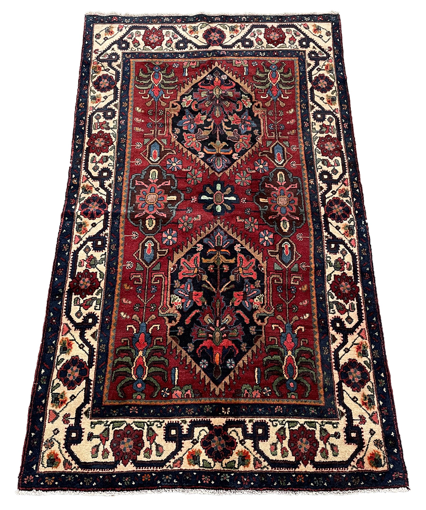 Persian Hamadan rug, the red ground field decorated with two floral medallions and stylised flower heads, repeating guarded border