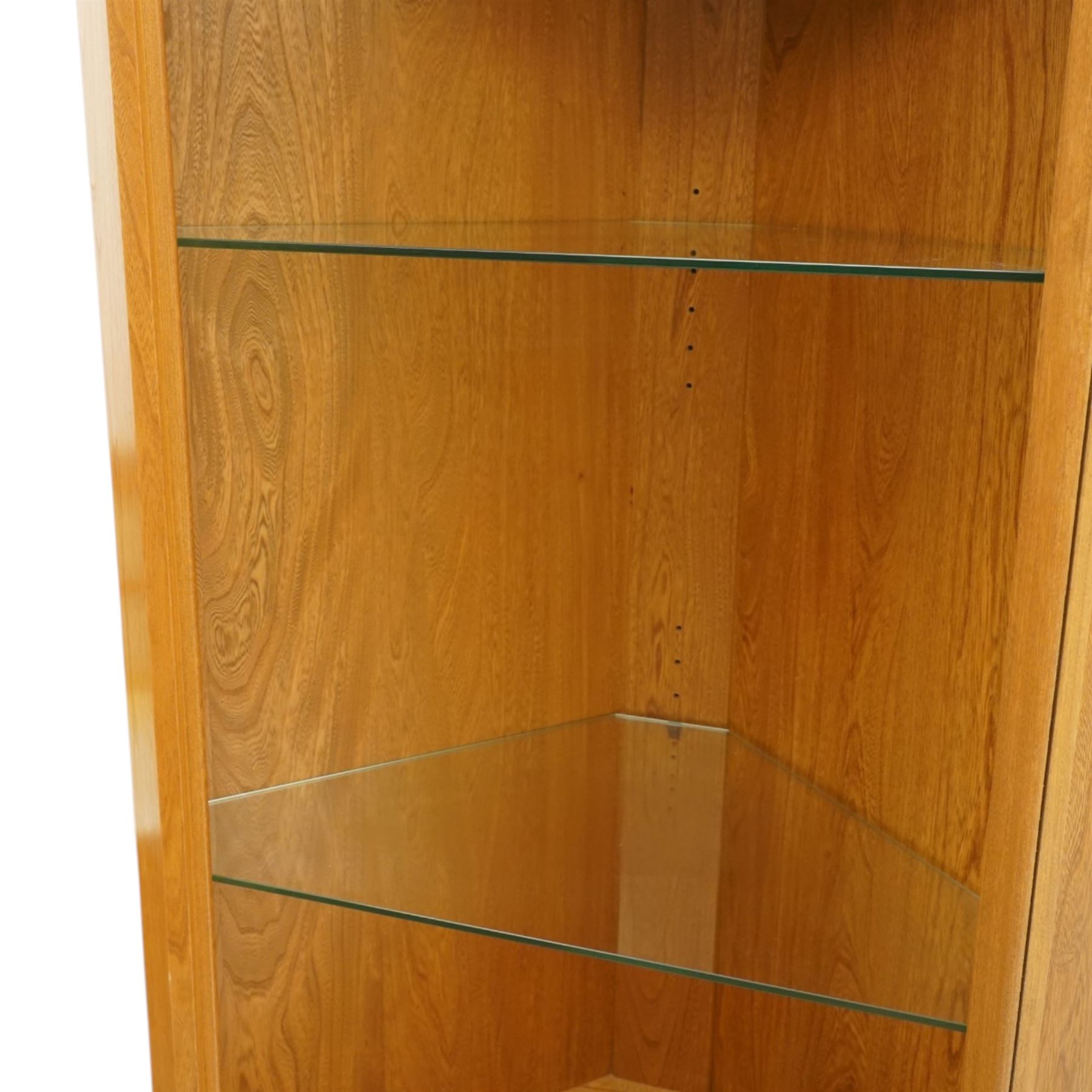 Ercol - elm corner display cabinet, Model 3856. Glazed upper section with glass door enclosing two glass shelves and interior light, above panel cupboard door, with rounded uprights and circular turned handles, on plinth base