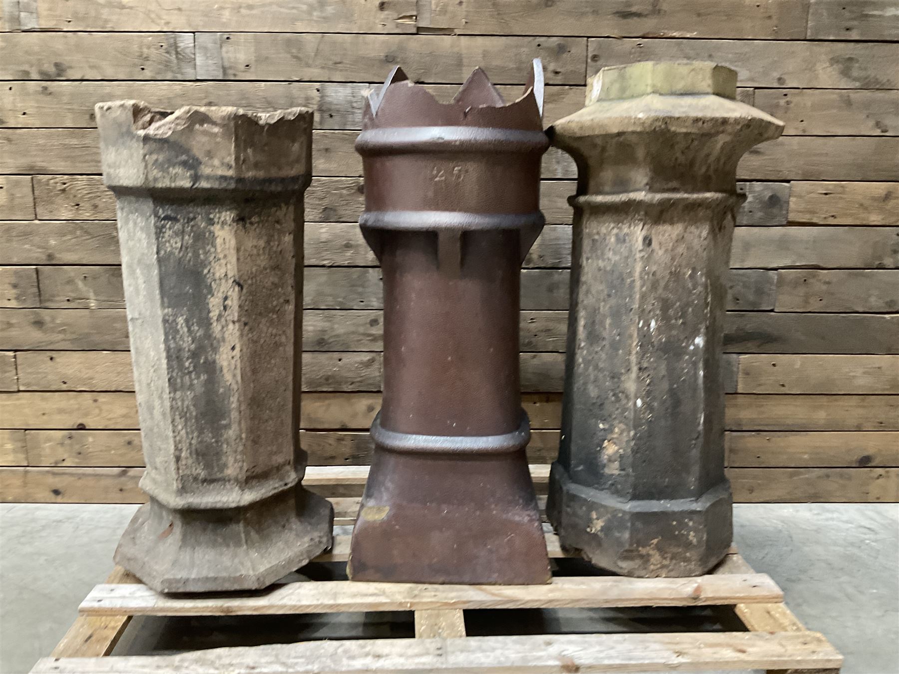 Collection of three Victorian and early 20th century reclaimed terracotta chimney pots, comprising: one cylindrical form with weathered, cracked glaze and flared octagonal base; one deep red cylindrical pot with fluted midsection and castellated rim, bearing moulded number ‘25’; and one tapering hexagonal example with wide flared rim and weathered patina. All with age-related wear and chips, consistent with use and outdoor exposure. Plus a selection of cast stone pieces including fountain 