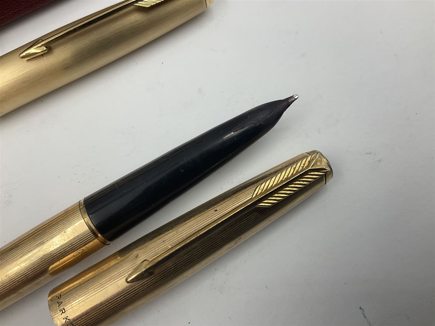 Three rolled gold Parker fountain pens, comprising an example with a gold nib marked 14K 585 and barrel with a shell stamp, a Parker 61 fountain pen with inset gold arrow to the nib, and another similar, all with striated decoration and arrow clips to the caps, L13cm, one with box