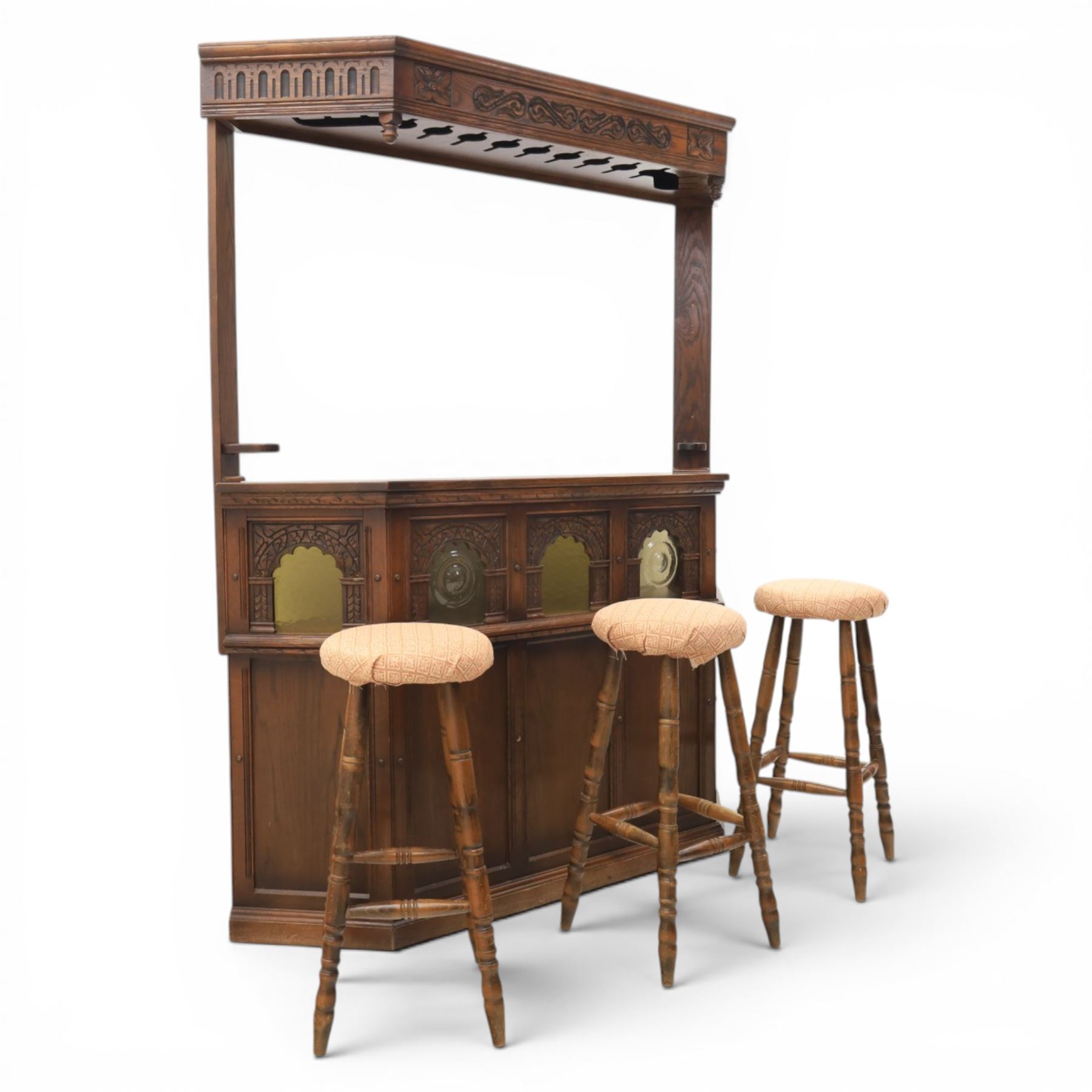 Old Charm - carved oak bar with three bar stools and associated Old Charm drinks cabinet, carved top with channels for glassware beneath, bar surface above glazed panels, shelves for glassware to the back, associated Old Charm drinks cabinet with fall front linenfold carving, above twin doors with shelved interior