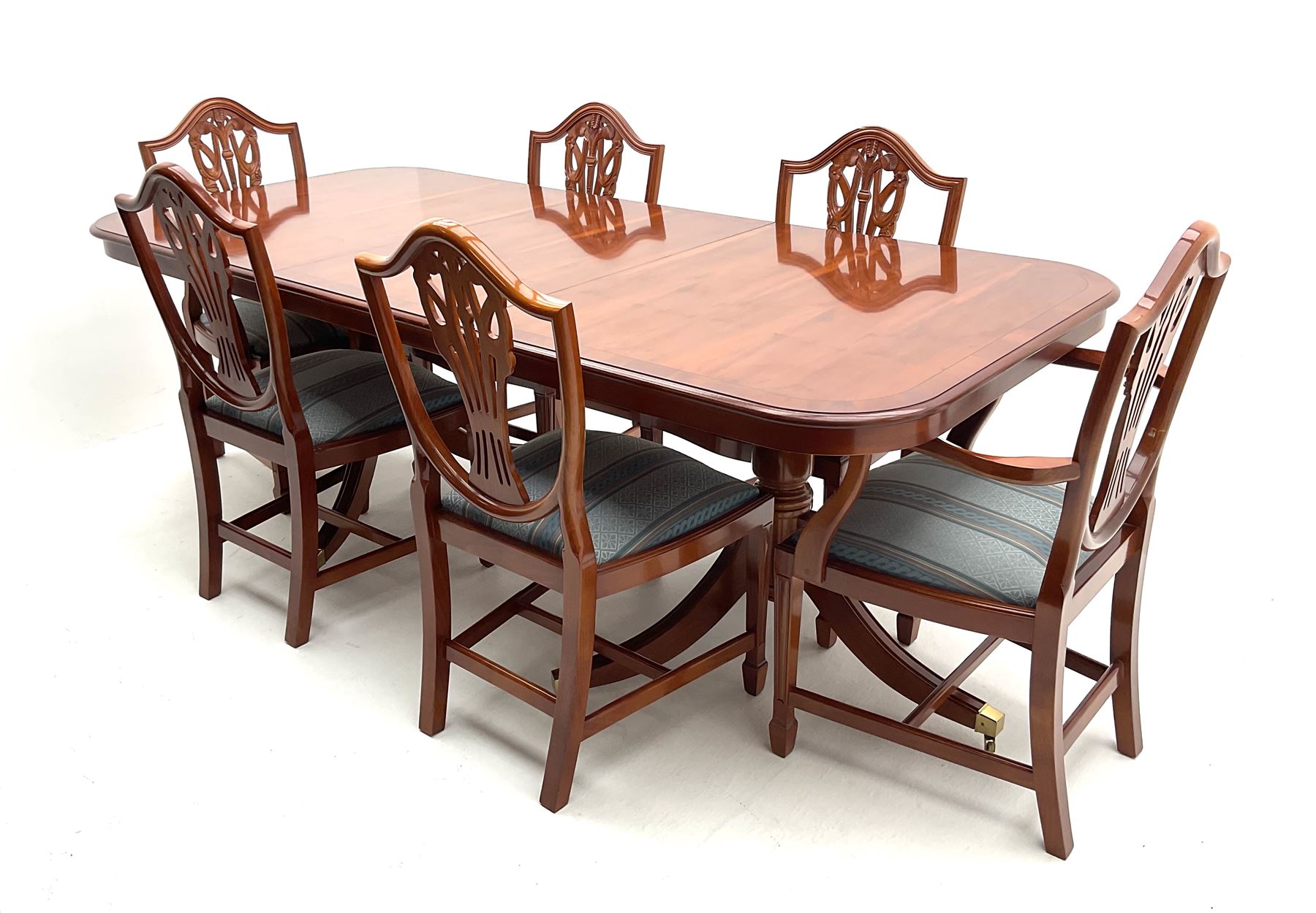 Yew wood twin pedestal extending dining table, shaped supports and brass castors (W216cm, D100cm, H77cm) and six (4+2) chairs, shaped back and upholstered in patterned fabric raised on fluted supports (W52cm)