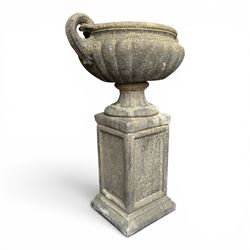 Pair of Neoclassical design weathered cast stone garden urns of kylix form, the rolled rim flanked by twin pierced scroll handles over a shallow gadrooned bowl, raised on a fluted circular socle and faux panelled square pedestal base