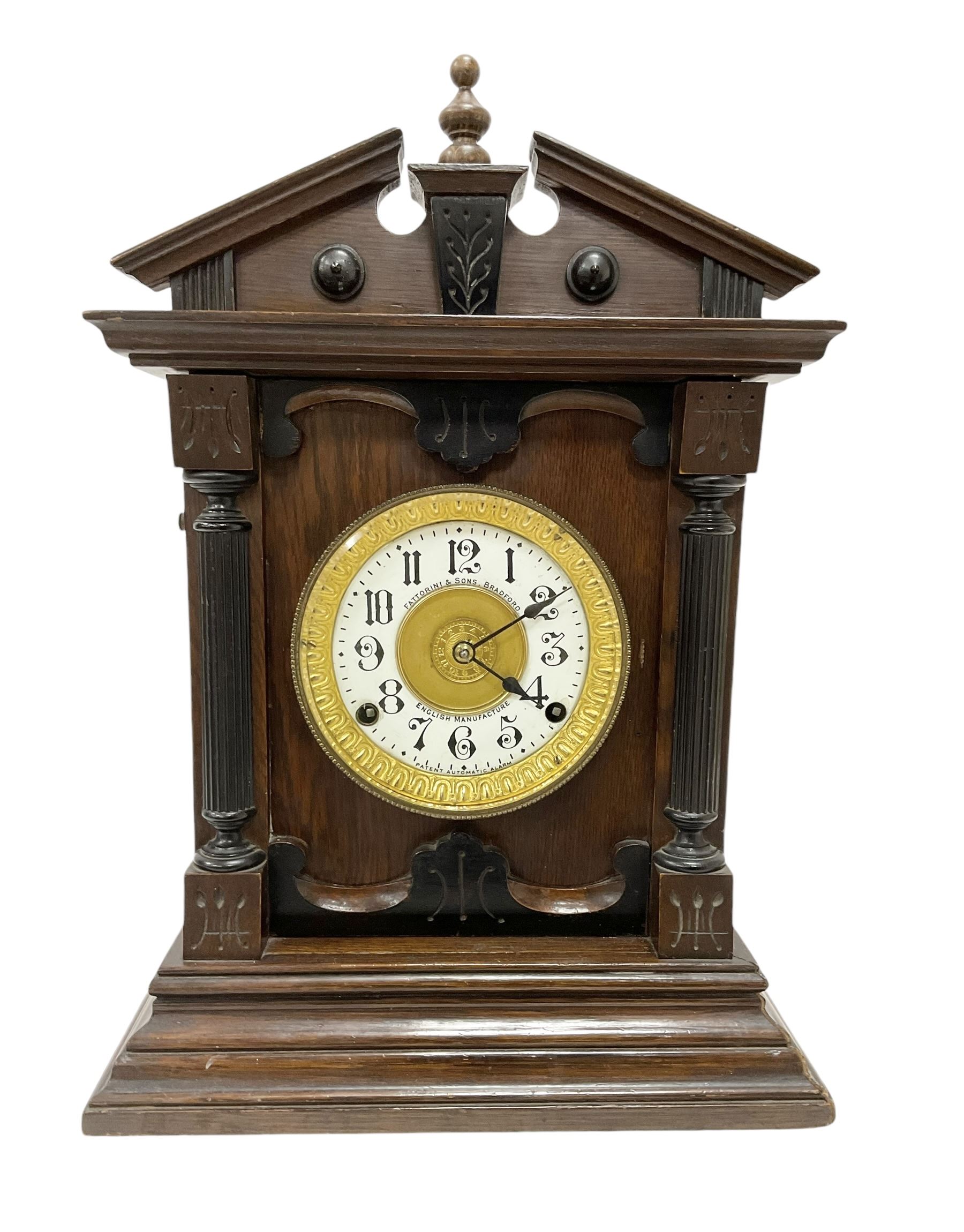 Fattorini of Bradford - oak cased early 20th century mantle clock with alarm, rectangular case with a broken pediment, turned finial and matching carved pilasters to the front, on a broad stepped plinth with a flat base, circular dial with an ivorine chapter within a decorative gilt bezel, Arabic numerals , spade hands and alarm setting disc to the centre, two train spring driven movement striking a coiled gong and bell. With key and pendulum. 