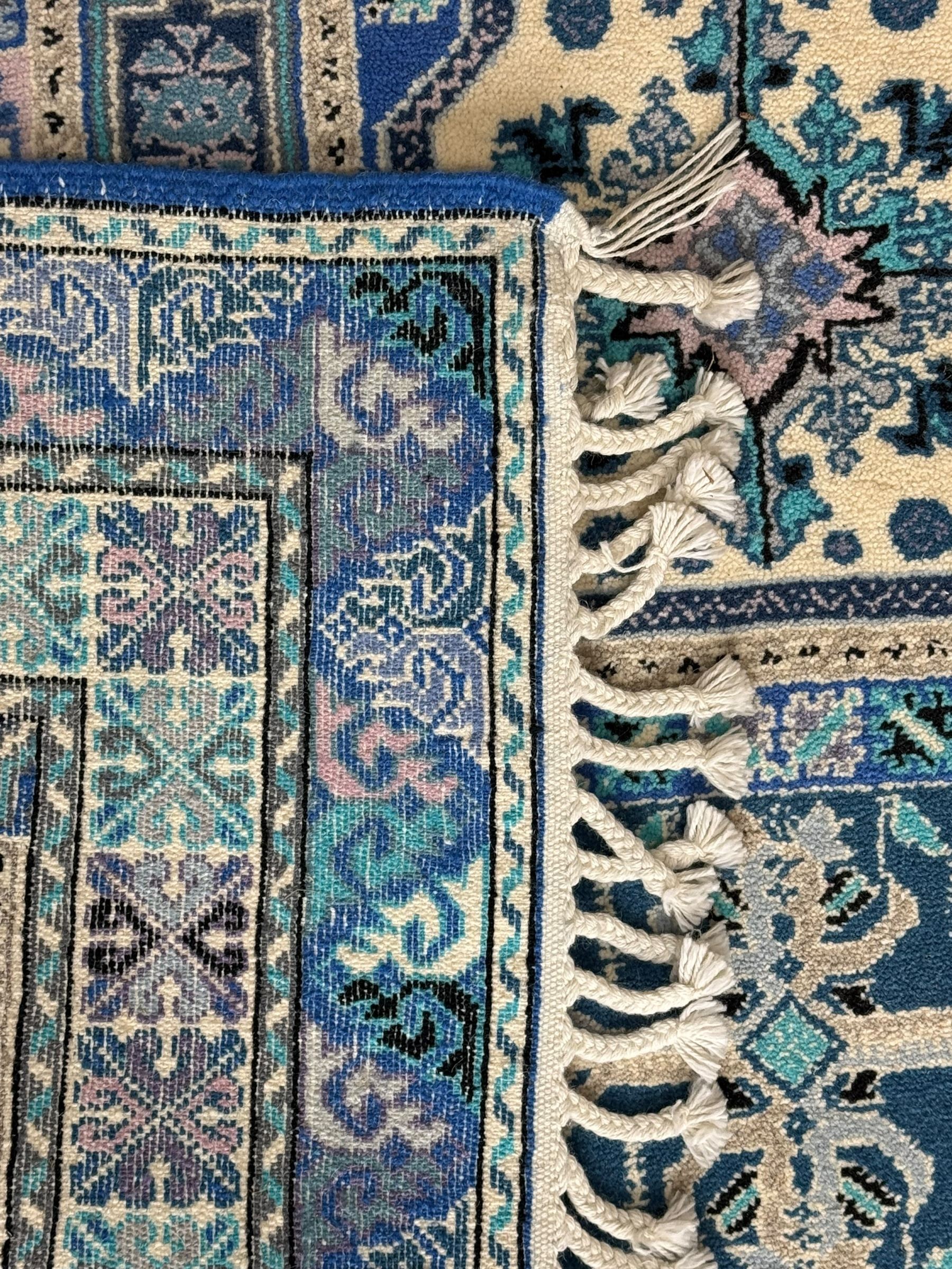 Morrocan single weft blue ground rug, the field segmented into a grid of ten rectangular panels, bordered by a series of guard bands with repeating floral and geometric patterns with interlocking vines and rosettes, the edges finished with a fringe of twisted tassles