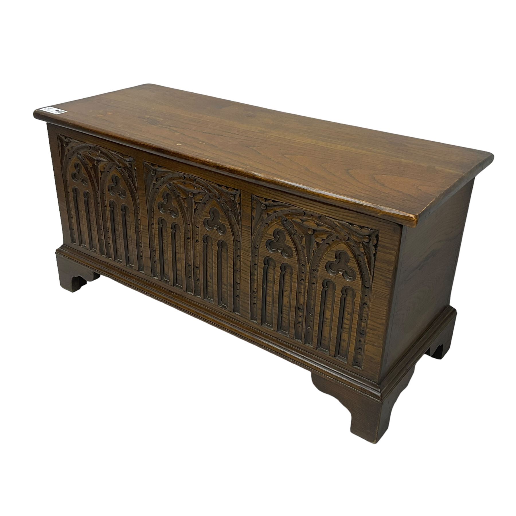 Mid-20th century oak blanket box, hinged lid over front carved with Gothic tracery work and flower heads, on bracket feet