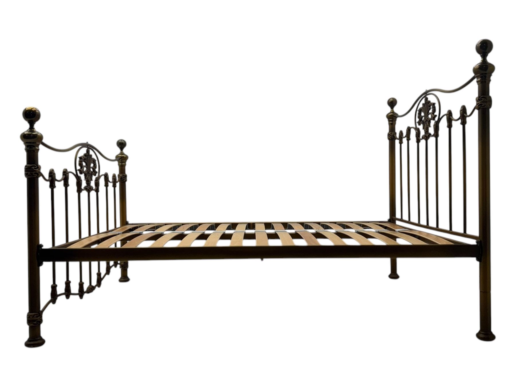 Victorian design king size brass bed frame, featuring an arched headboard and footboard with intricate cast floral and scrollwork centre motifs, flanked by cylindrical supports with ball finials and decorative collars, raised on rounded feet, with a slatted wooden base