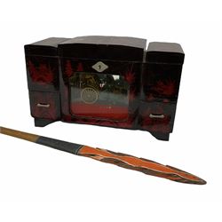 Oriental lacquered jewellery box, the body decorated with a black and red mountainous riverscape enclosing a glass compartment with simulated ivory rickshaw figure and three hinged lids opening to reveal mirror and various compartments and painted ceremonial stick