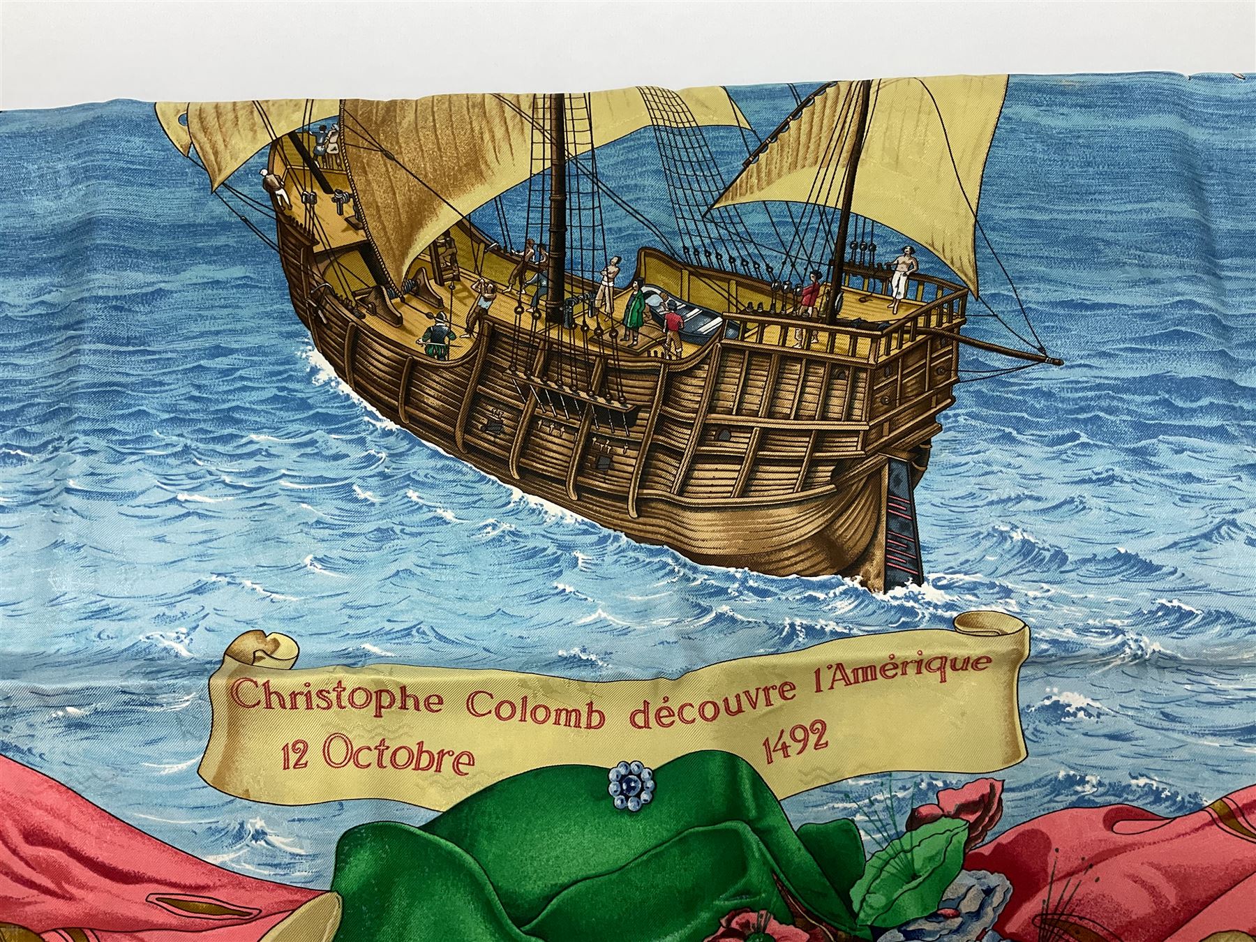 Hermès 'Christophe Colomb Découvre l'Amérique' jacquard silk scarf, designed by Carl de Parcevaux in 1992, limited edition for the bi-centenary of the discovery of America, printed with a central image of Christopher Columbus' ship at sea, surrounded with colourful stylised feathers, birds, flags, globes, shells and flowers, contained within vibrant red border, with rolled hand stitched edges and Hermes material label, 87cm square