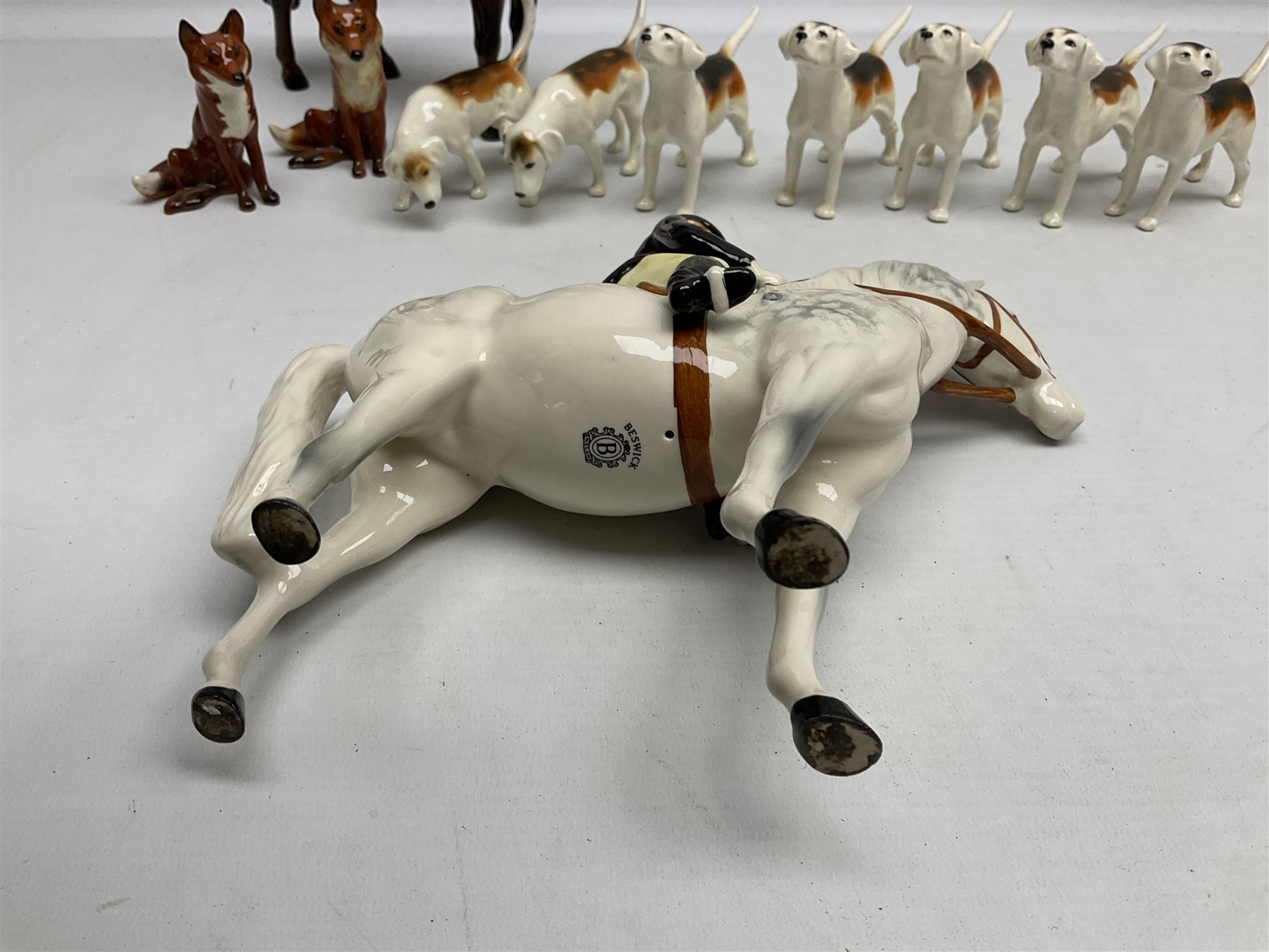 Beswick hunting group, comprising huntswoman on grey horse no 1730, huntsman on brown horse no 1501, two seated fox figures no 1748 and seven fox hounds, all with printed marks beneath (11)