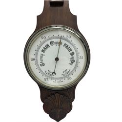 An English carved oak cased aneroid barometer with an 8'' porcelain dial, measuring barometric pressure from 26 to 31.9 inches, weather predictions written in gothic capitals and lower-case script, with a steel indicating hand and brass recording hand within a chrome bezel with a flat bevelled glass, with a spirit thermometer recording the temperature in degrees Fahrenheit and Celsius.



