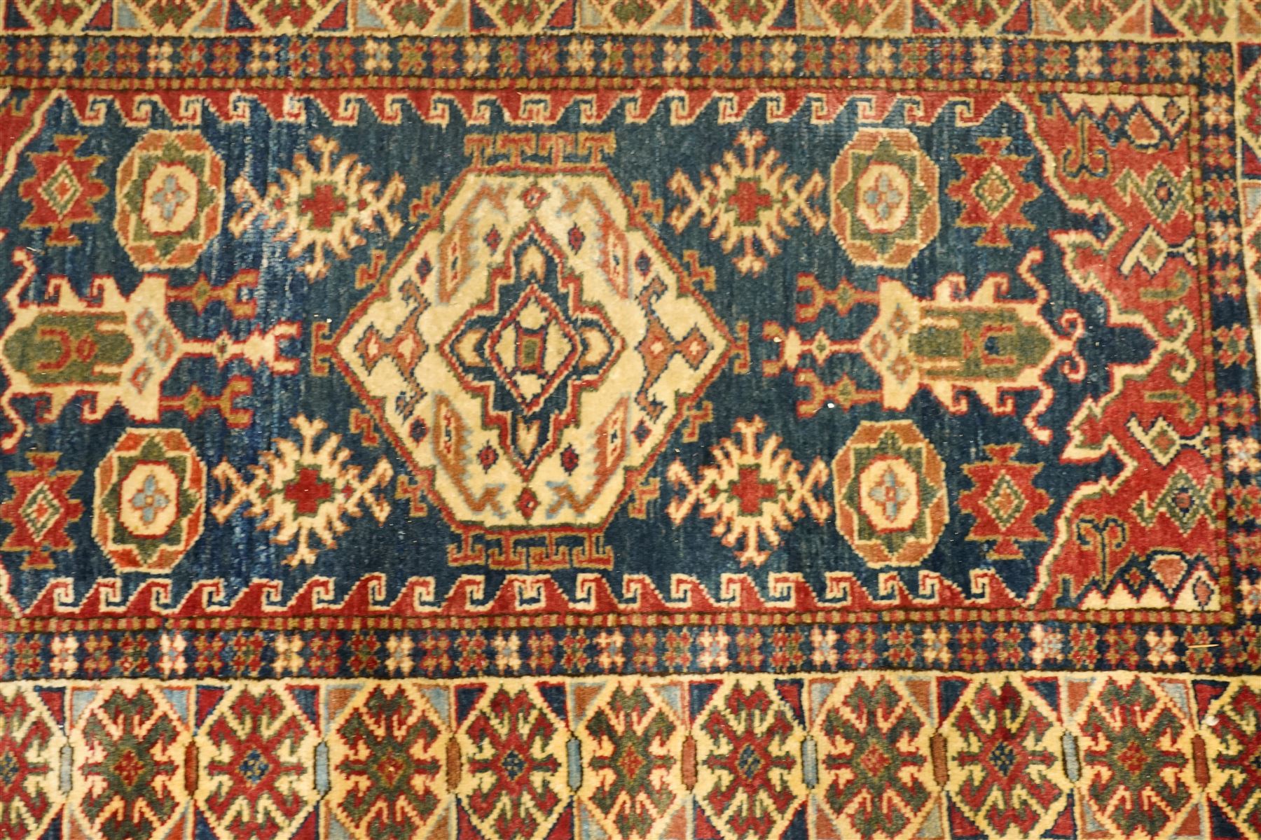 Caucasian hand-knotted runner, dark navy ground with three ivory geometric medallions surrounded by stylised flowerheads and angular motifs in madder red, green and ivory, enclosed by repeating geometric borders