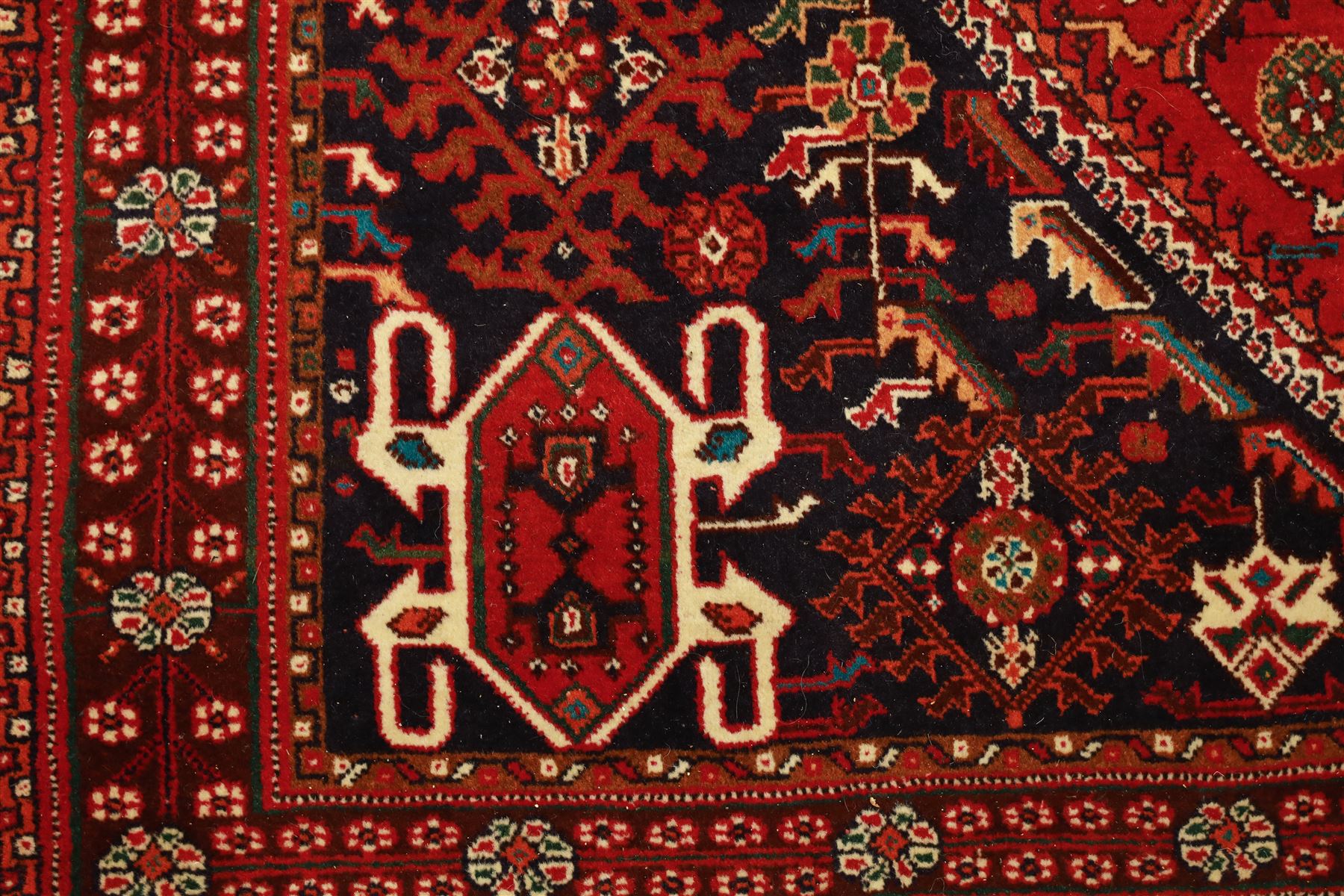 Persian tribal hand-knotted rug, crimson ground, madder field with central stepped lozenge medallion with scattered floral and geometric spandrels with rosette border 