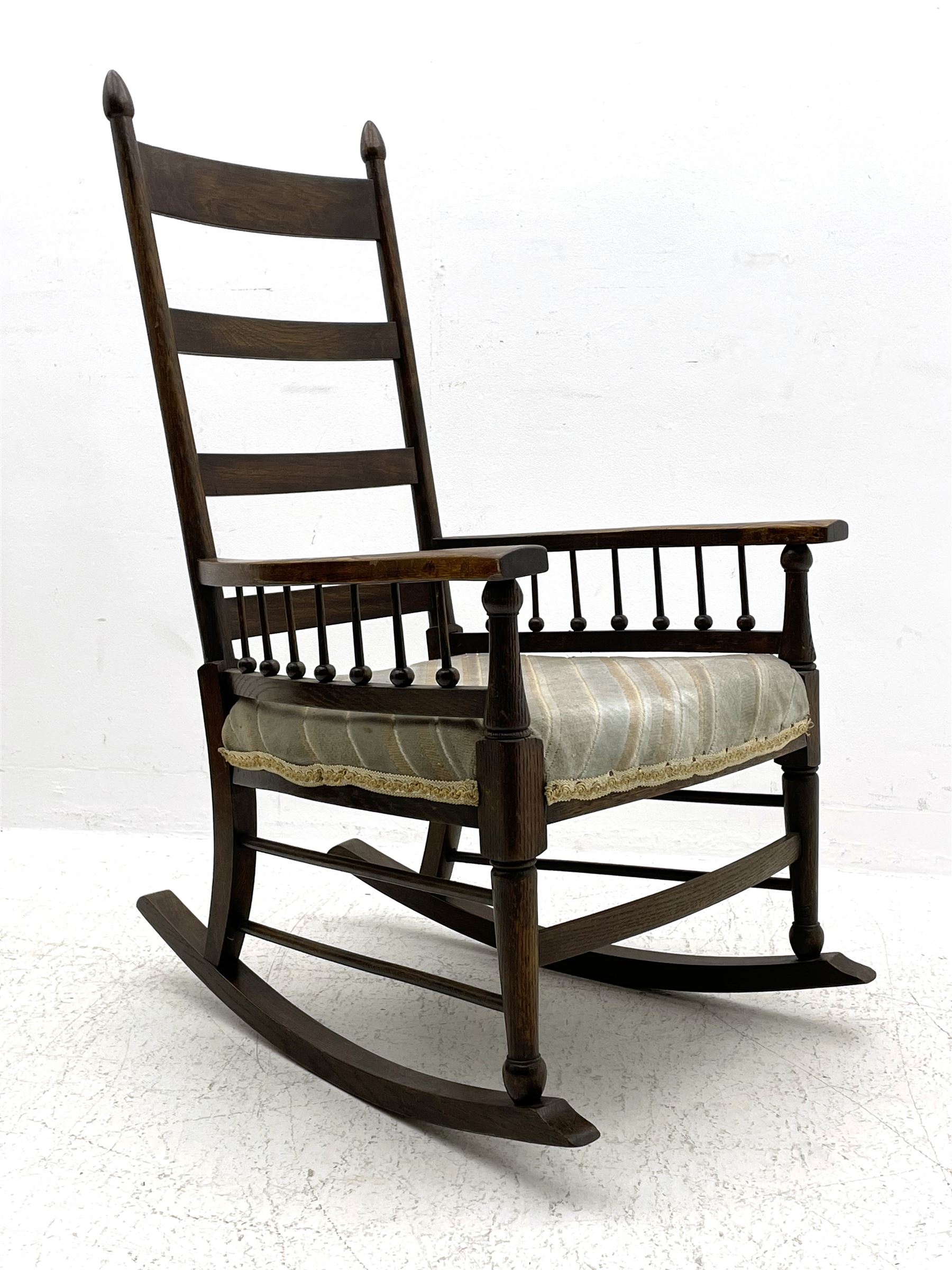 William Birch for Liberty & Co. - Arts and Crafts period oak ladder back rocking chair, the arms supported by a series of turned spindles, upholstered seat