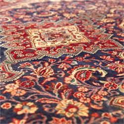 North West Persian hand-knotted Sarouk rug, central navy ground field with cusped lozenge medallion with pendant motifs, scrolling palmettes, and floral sprays, cream spandrels, and madder red border of stylized rosettes and leafy meandering vines between multiple guard stripes 