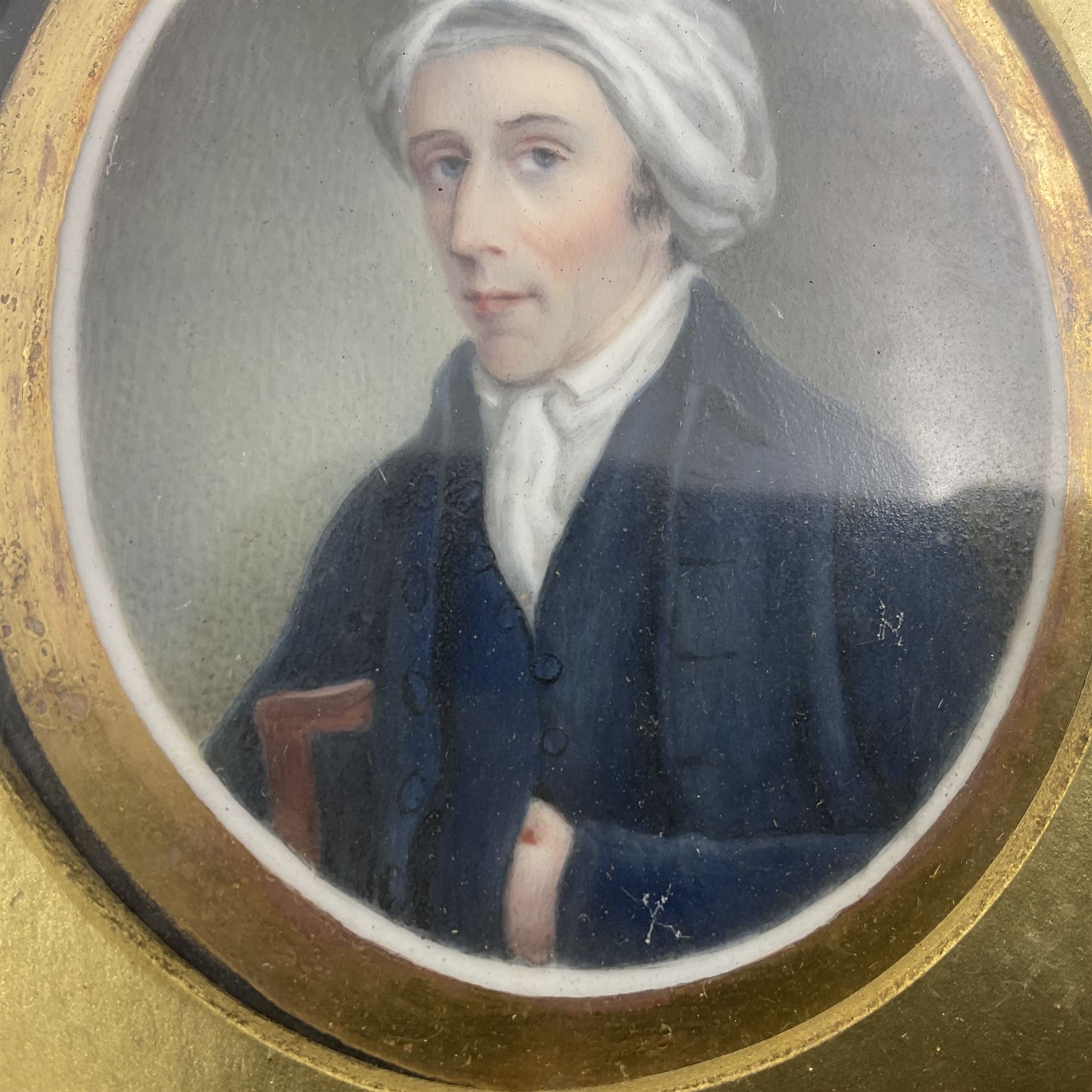 English School (18th century)
Portrait miniature upon ceramic plaque 
Head and shoulder portrait of a gentleman in blue coat and white turban, holding book under one arm
Indistinct inscription verso
Within gilt mount and gilt frame under glass
Portrait 7cm x 5.5cm 
Plaque 14cm x 11.5cm
Frame 16cm x 13.5cm