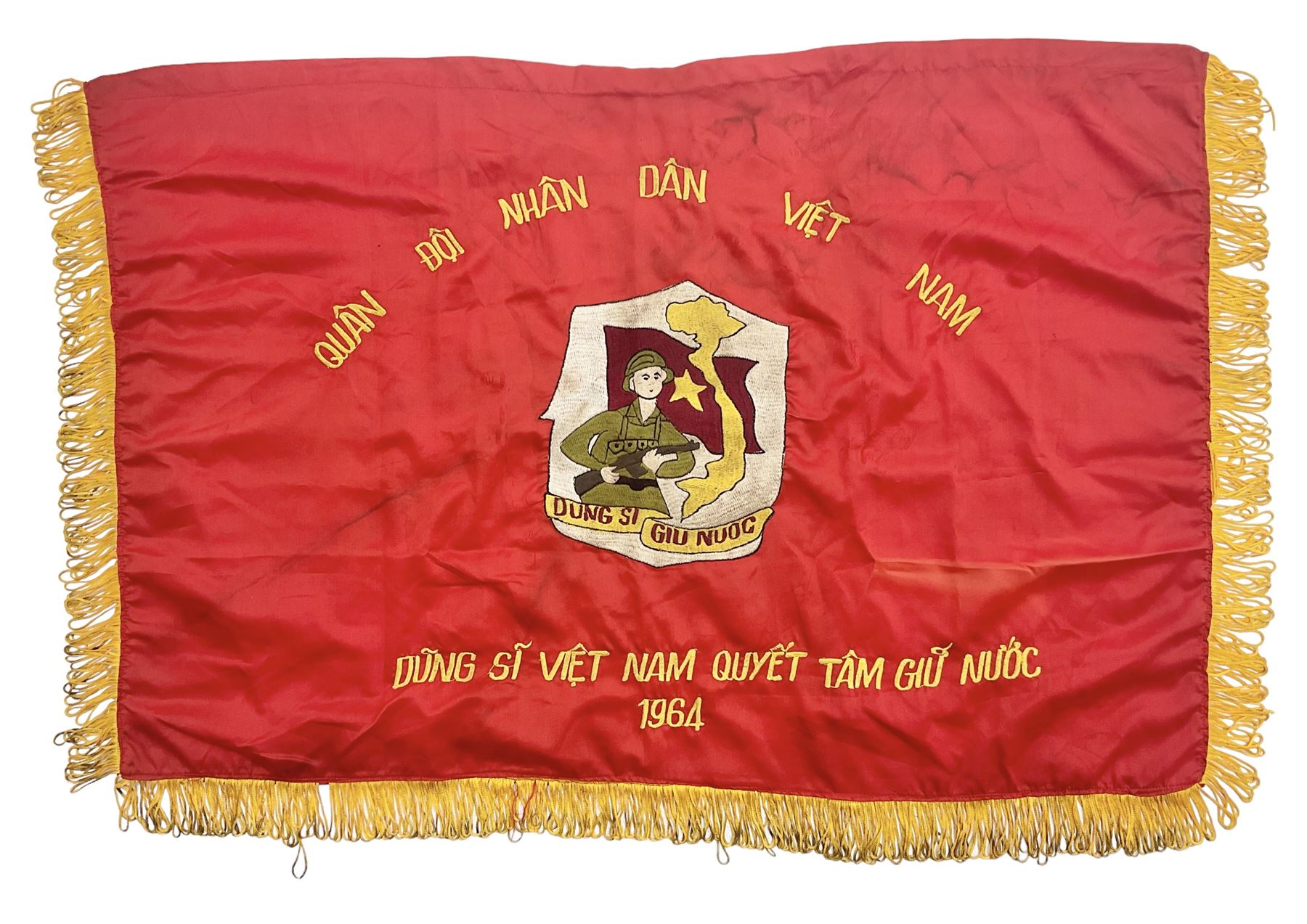 1960s North Vietnam banner embroidered in yellow thread on a red ground, roughly translates as 'Peoples Army of Viet Nam. Warriors of Viet Nam Determined To Keep The Country 1964' around a central military crest with the motto 'Warriors Keep The Country'; tassels to three sides 70 x 100cm