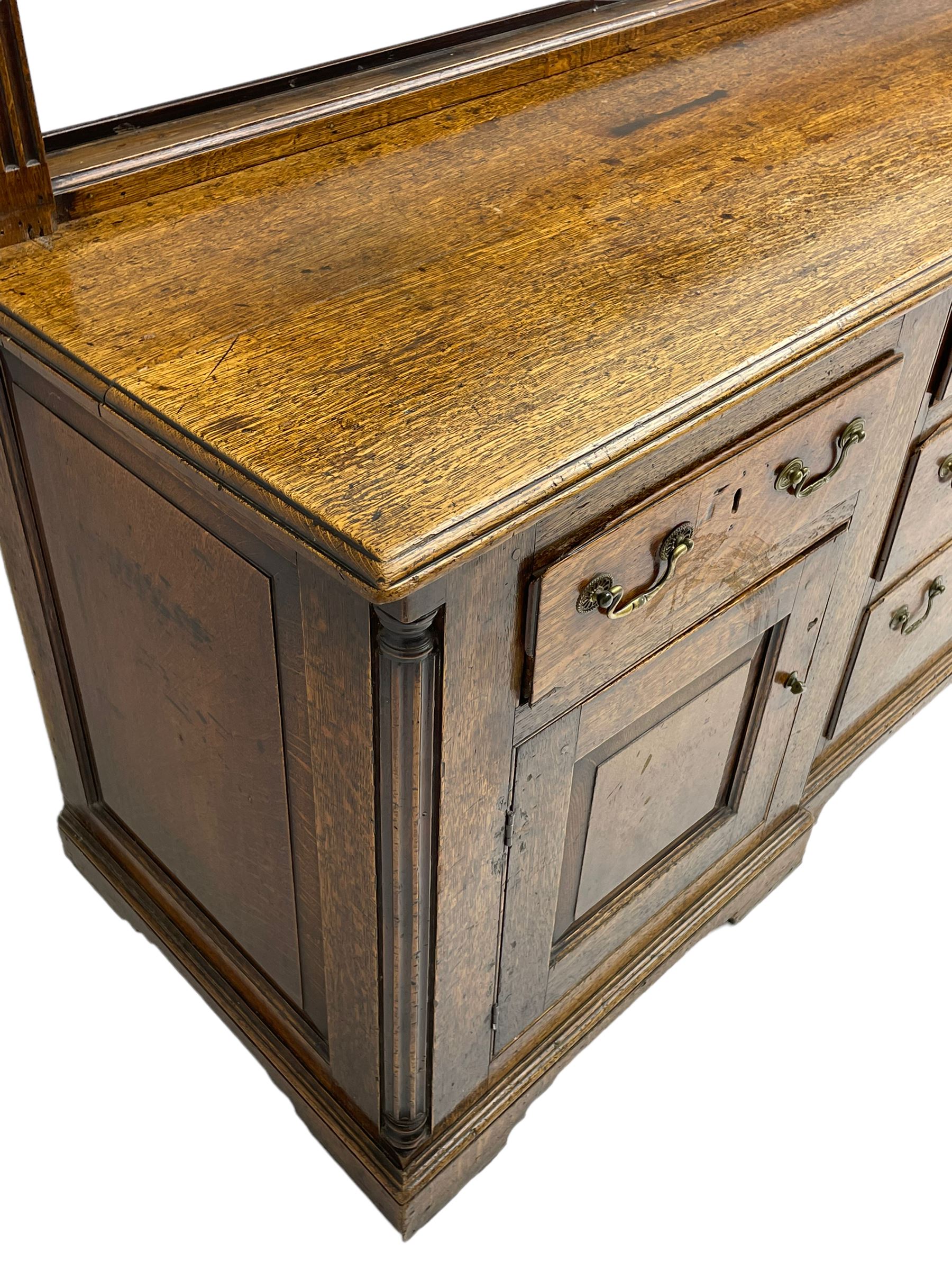 George III oak dresser, projecting dentil cornice over three heights plate rack enclosed by fluted uprights, the dresser fitted with five drawers and two panelled cupboards, canted corners with fluted quarter columns, on bracket feet