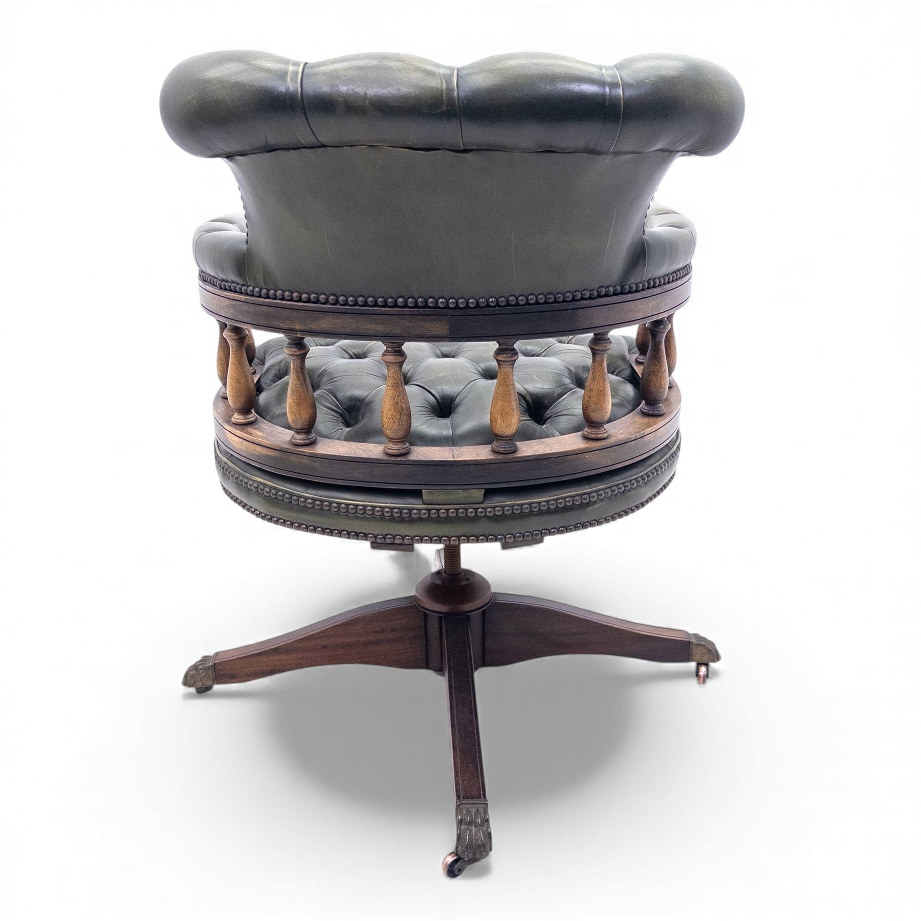 Mid 20th century buttoned green leather office chair, the curved back and arms over a circular frame with turned spindle supports, on a revolving base with four splayed legs and brass castors