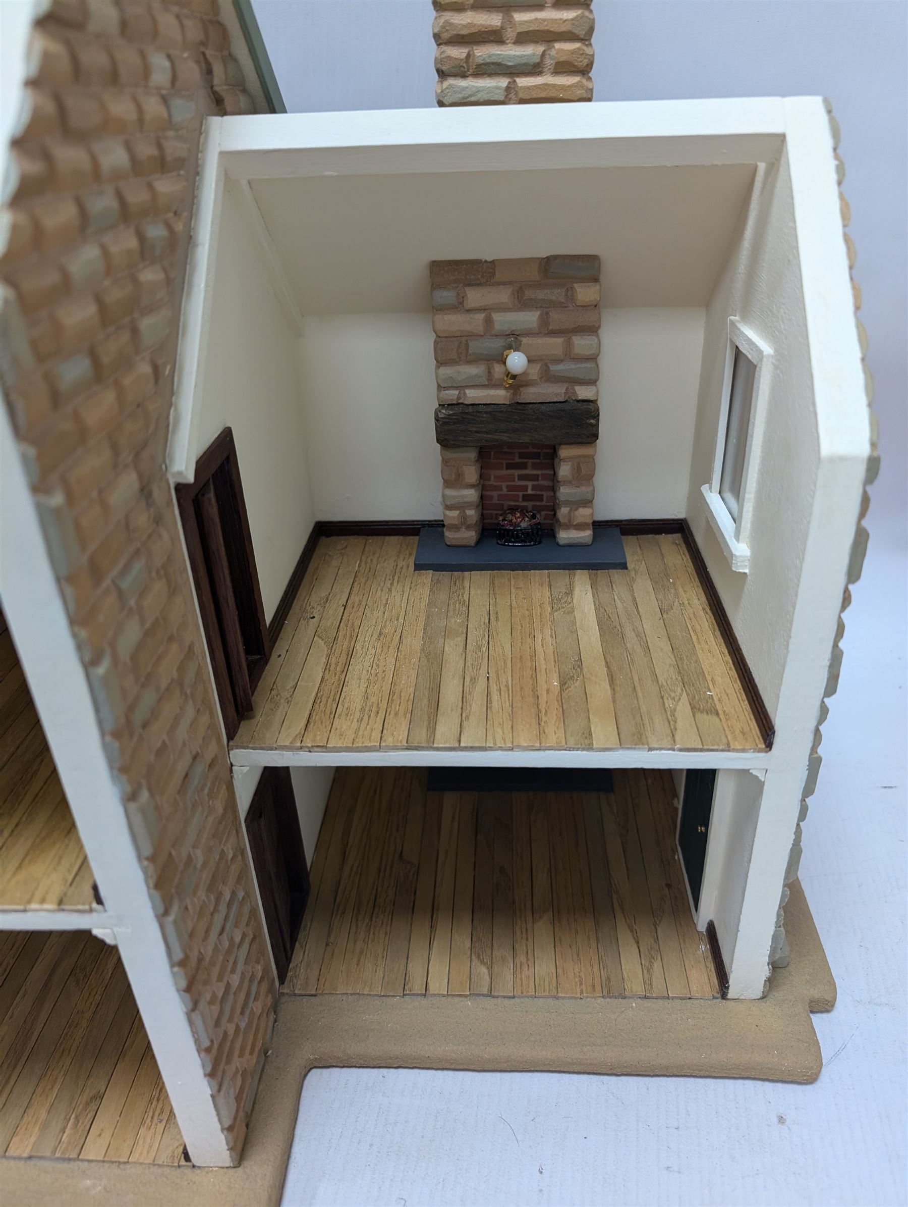 1:24 scale stone effect three-storey cottage dolls house, with green arched door and lattice effect windows, decorated to the interior with wooden floors, wired lighting and fire places, H45cm, W57cm, D26cm