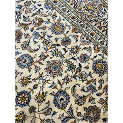 Persian Kashan Ivory ground carpet, the busy field decorated all over palmettes and trailing branches, scrolling border interspersed with stylised plant motifs, within guard stripes