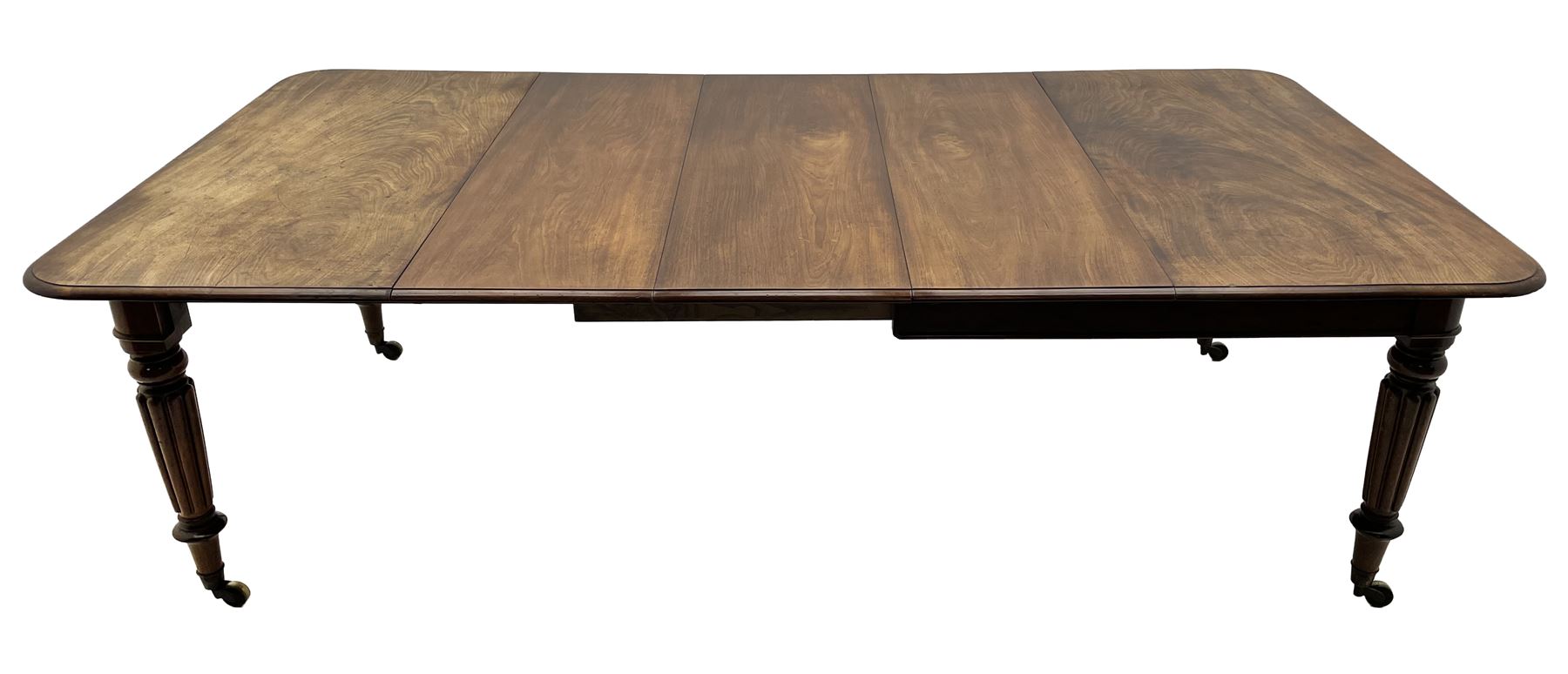 Early 19th century figured mahogany extending dining table, the rectangular top with moulded edge and rounded corners, pull-out action with three additional leaves, raised on turned and lobe carved supports with brass cup castors