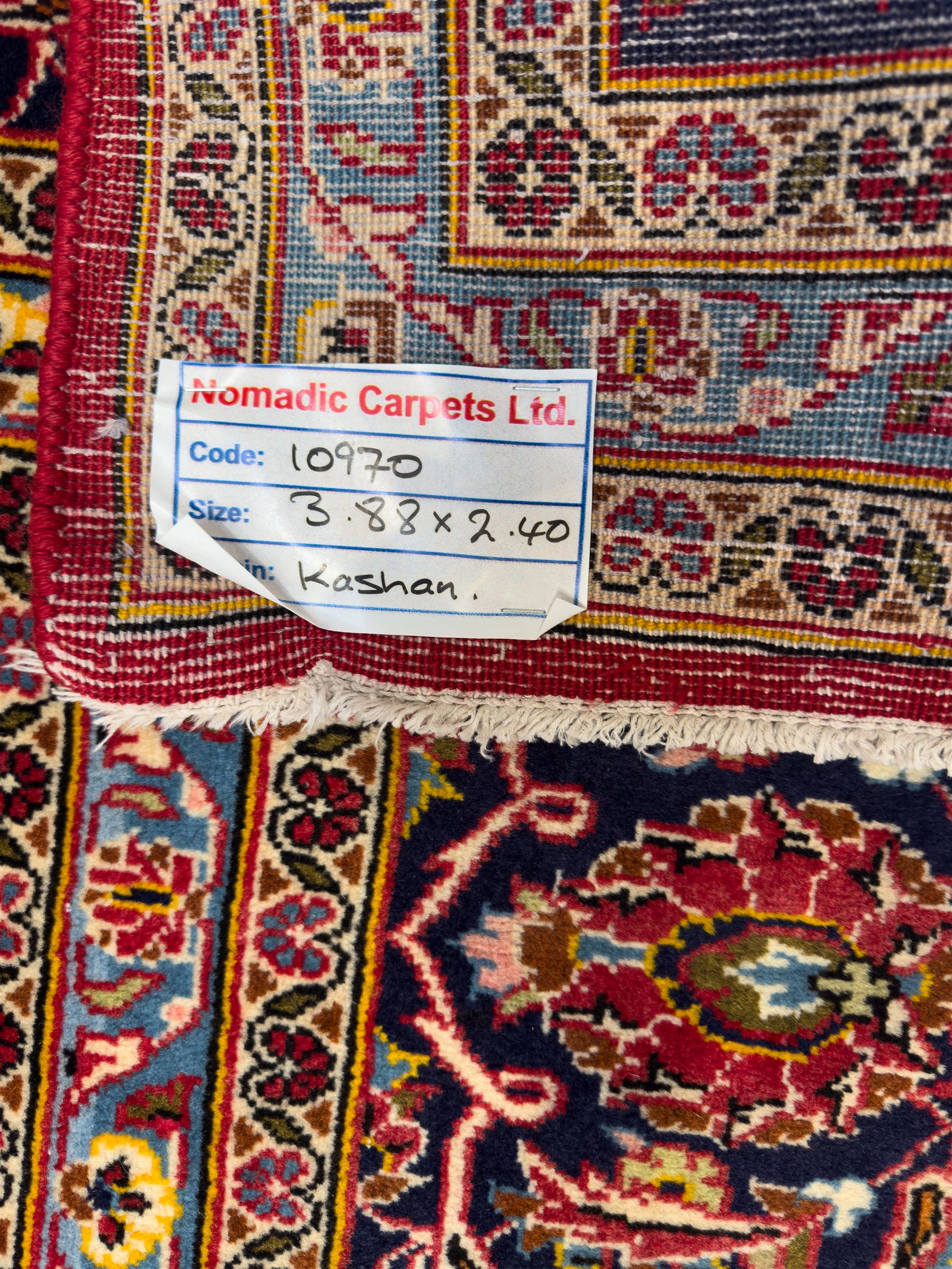 Central Persian Kashan hand-knotted carpet, the madder red field with central lobed medallion in indigo and ivory, enclosing scrolling arabesques and flowerheads, framed by palmette spandrels and an indigo border of rosettes and lotus forms between multiple floral guard stripes, from the region of Kashan