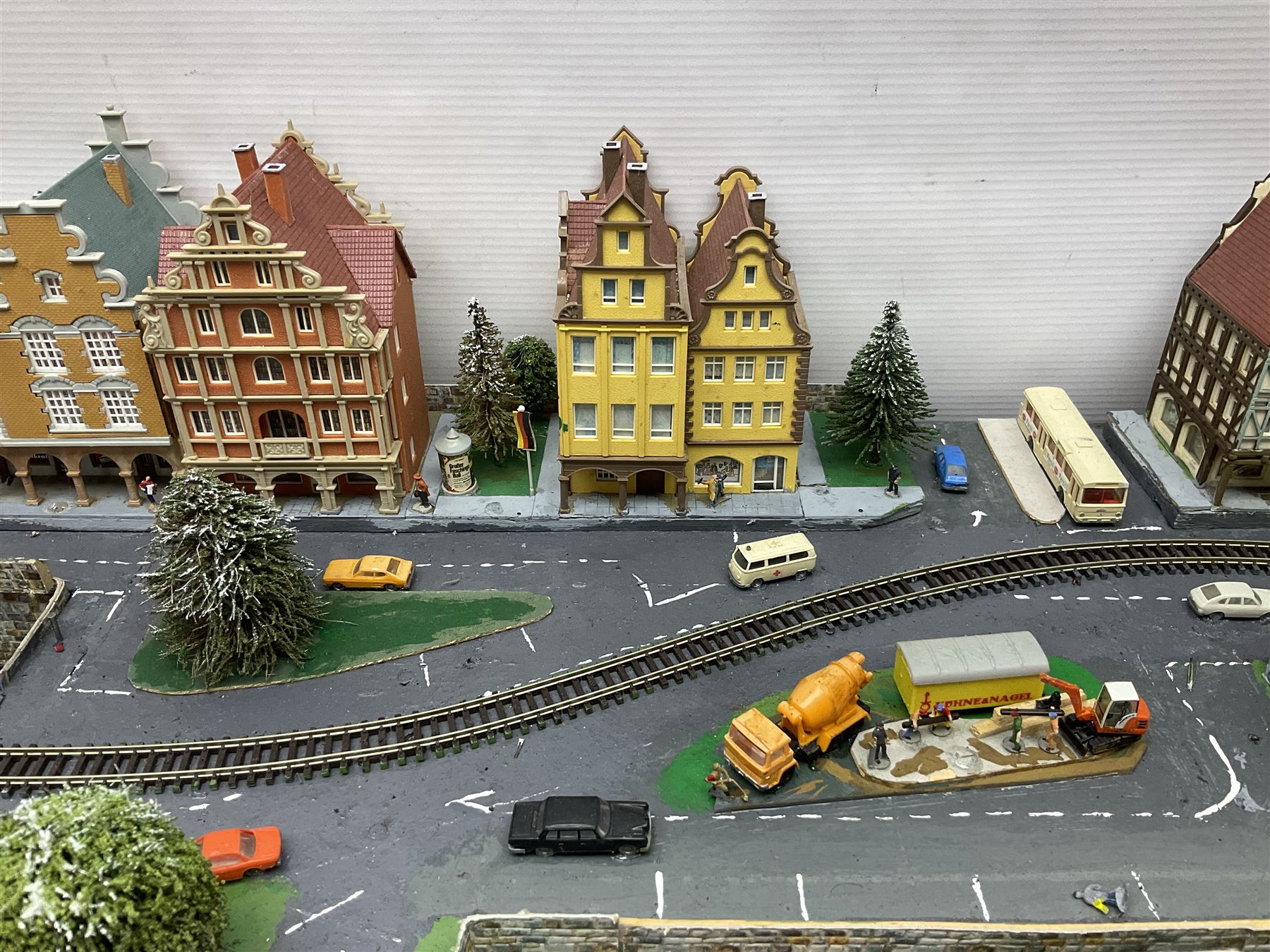 Table top 'N' gauge continental scenic layout as a split level town with various loops of track, station with numerous platforms, engine shed, assorted buildings, roads with motor vehicles and figures, tunnels, trees, river with bridge, tram depot etc 122 x 52cm