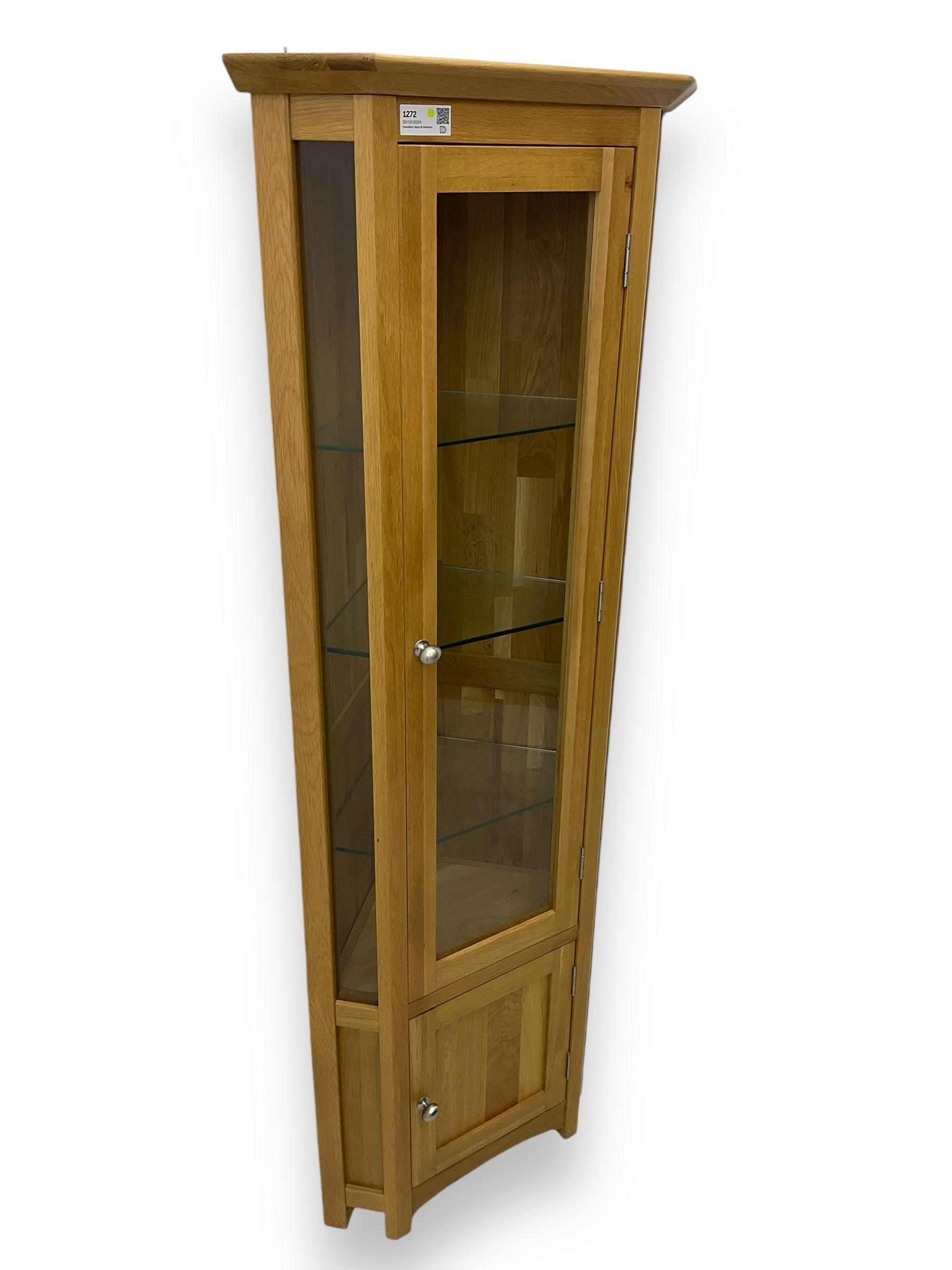 Contemporary light oak corner display cabinet, projecting cornice over single glazed door enclosing three glass shelves, the base fitted with panelled cupboard enclosing single oak shelf, on stile supports