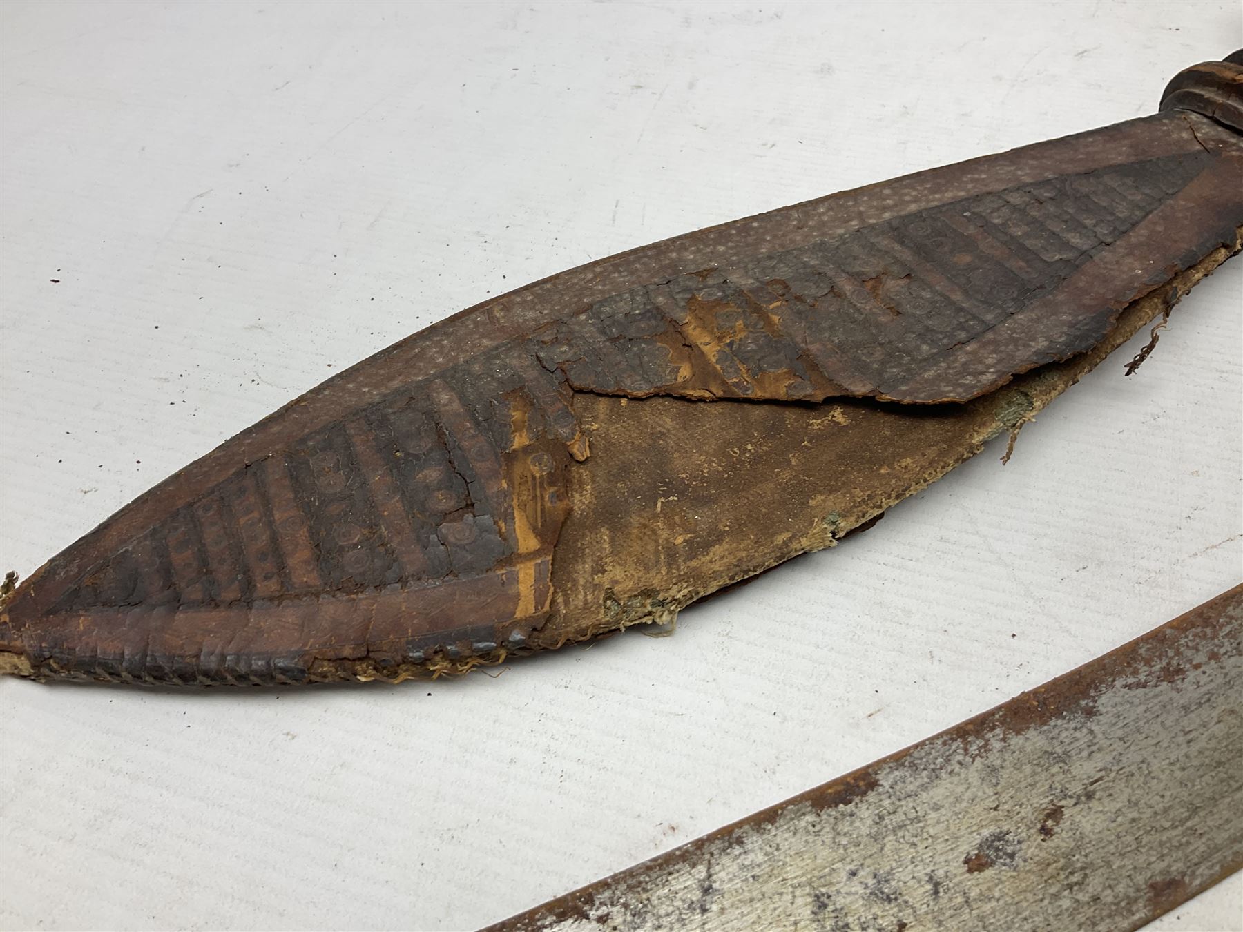 Mandingo sword, the 63cm plain curving steel blade marked with a horses head and the initials G.S.; leather covered grip with metal ribbed spherical pommel; in decorative leather leaf scabbard mounted with tassels and roundels L84cm overall; and a North African flyssa sword in poor condition with wooden scabbard (2)