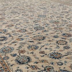 Large Central Persian Kashan hand-knotted carpet, ivory field with small central floral medallion issuing an all-over design of palmettes, rosettes, and scrolling vines enclosed by a complimentary foliate border framed by guard stripes, in a palette of ivory, power blues, and muted polychrome tones, with cotton fringe ends 