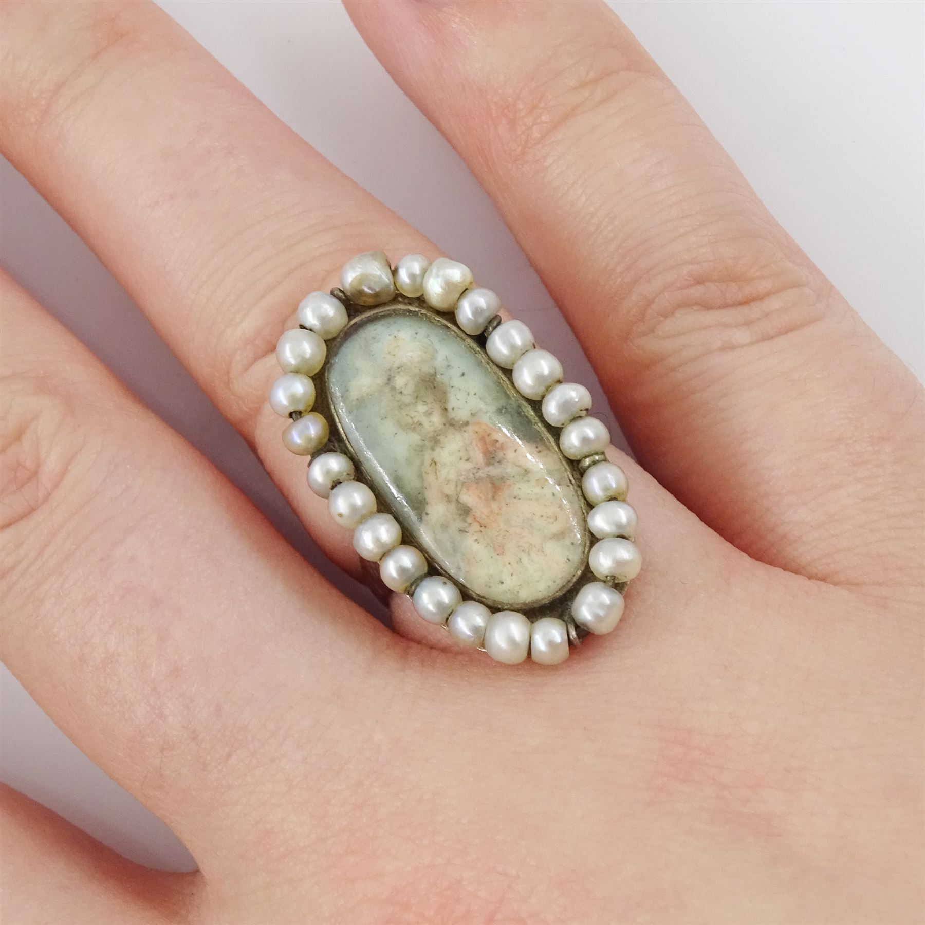 19th century portrait ring, set with an oval miniature of a woman wearing a pink dress on ivory, under a glazed panel, with threaded pearl surround and engraved shoulders. This lot has been registered for sale under Section 10 of the APHA Ivory Act