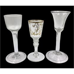 Three 18th century wine glasses comprising a plain stemmed glass with bell shaped bowl and conical folded foot H16cm, another plain stemmed glass with ogee bowl and folded foot and a Continental glass with gilt faceted bowl, decorated with male figure within a landscape, on a clear Silesian seven sided cut stem (3)