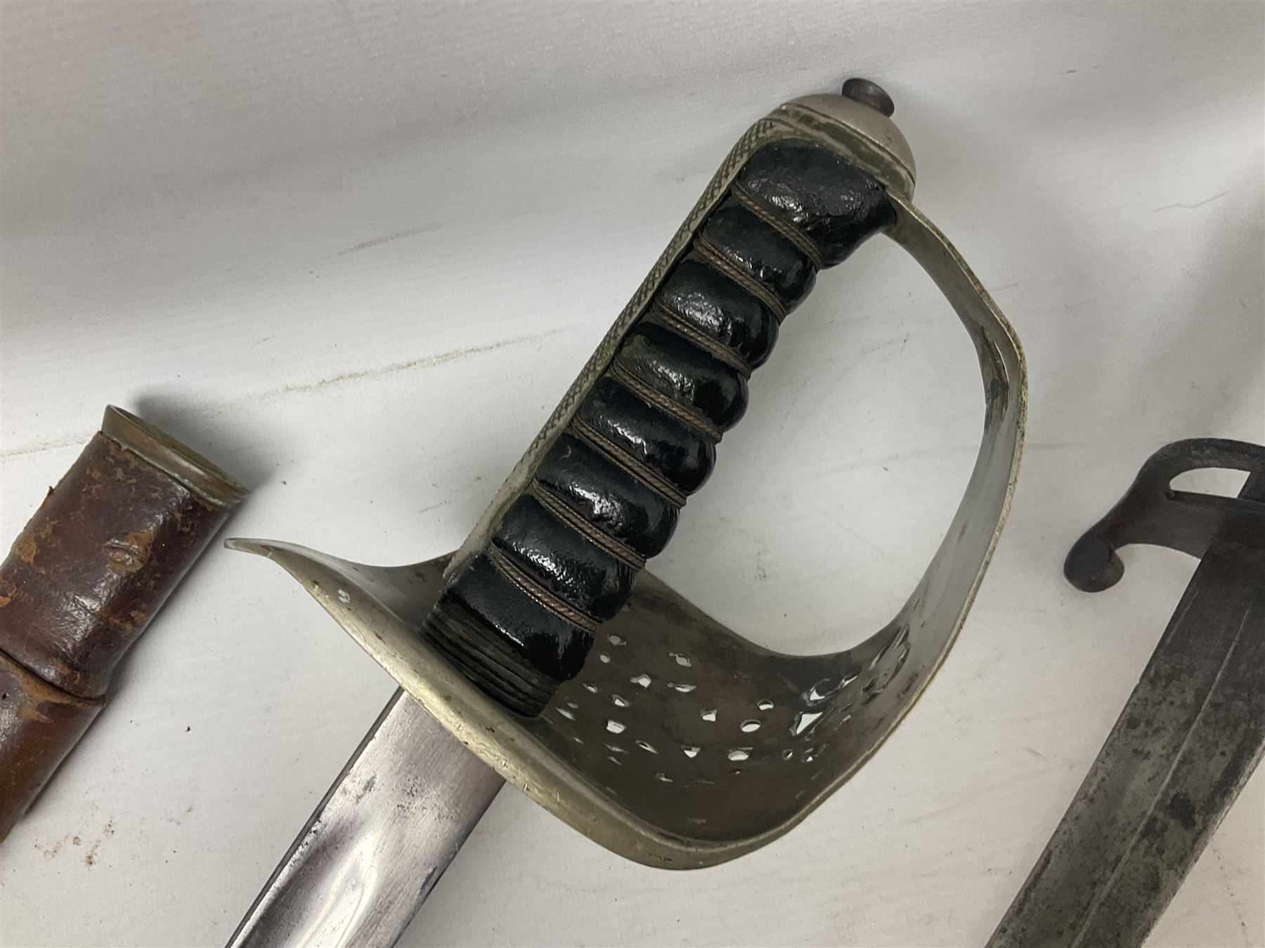 George V British Army 1897 pattern officers sword with plain 82cm fullered steel blade, pierced  basket hilt with George V cypher and wire bound leather grip with chequered backstrap; in leather covered field service scabbard L101cm overall; and another officer's sword in relic condition lacking scabbard (2)