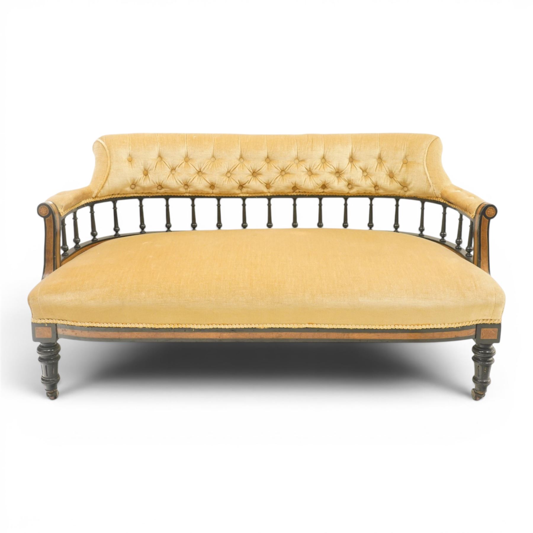 Late Victorian Aesthetic Movement settee, with buttoned upholstered roll-over back and arms, open spindle gallery frame with turned uprights, stuff-over seat, on shaped ebonised supports