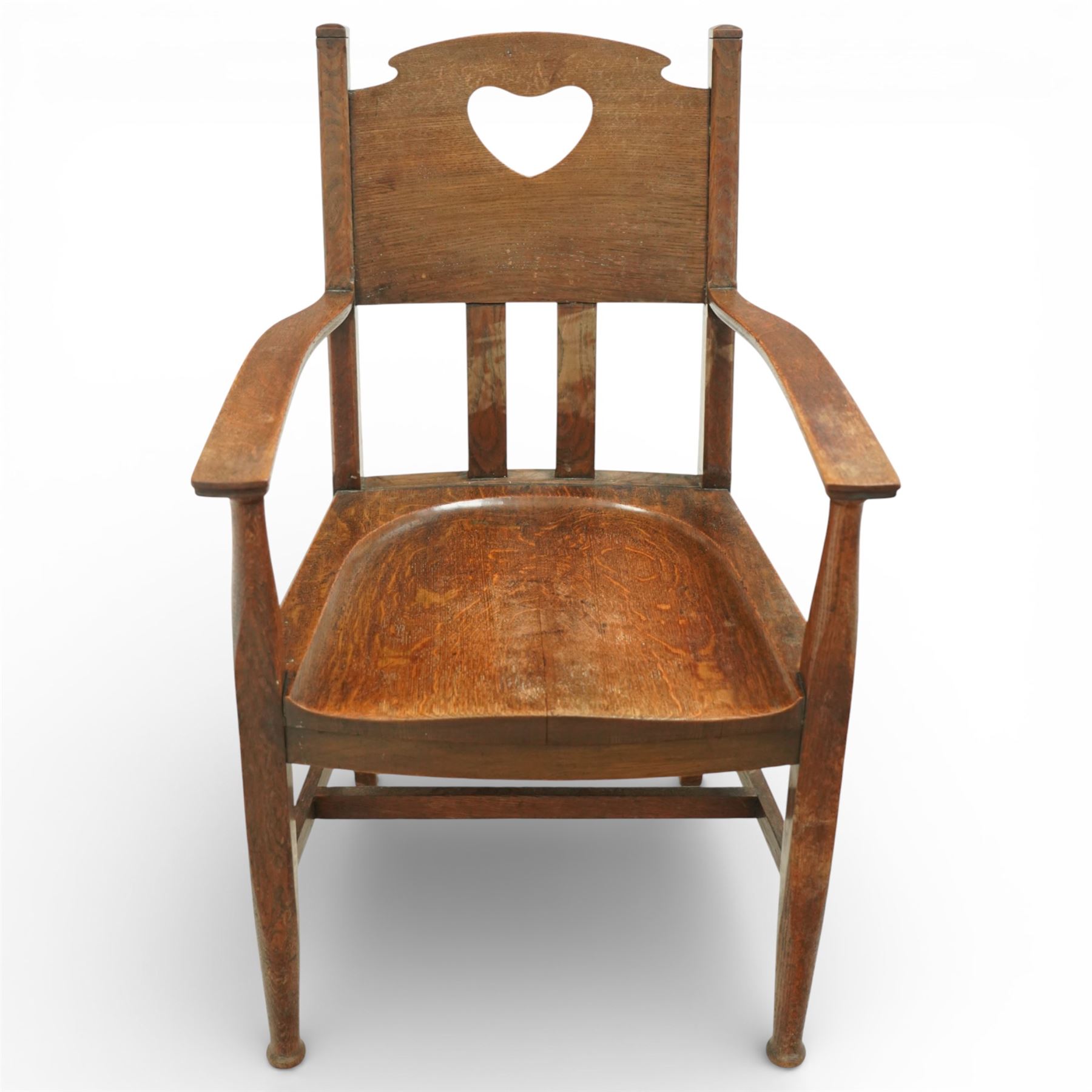 Arts and Crafts oak armchair, the shaped back with heart-shaped pierced splat above three vertical slats, solid dished seat with rounded front, open arms on turned front supports, square section legs united by plain stretchers